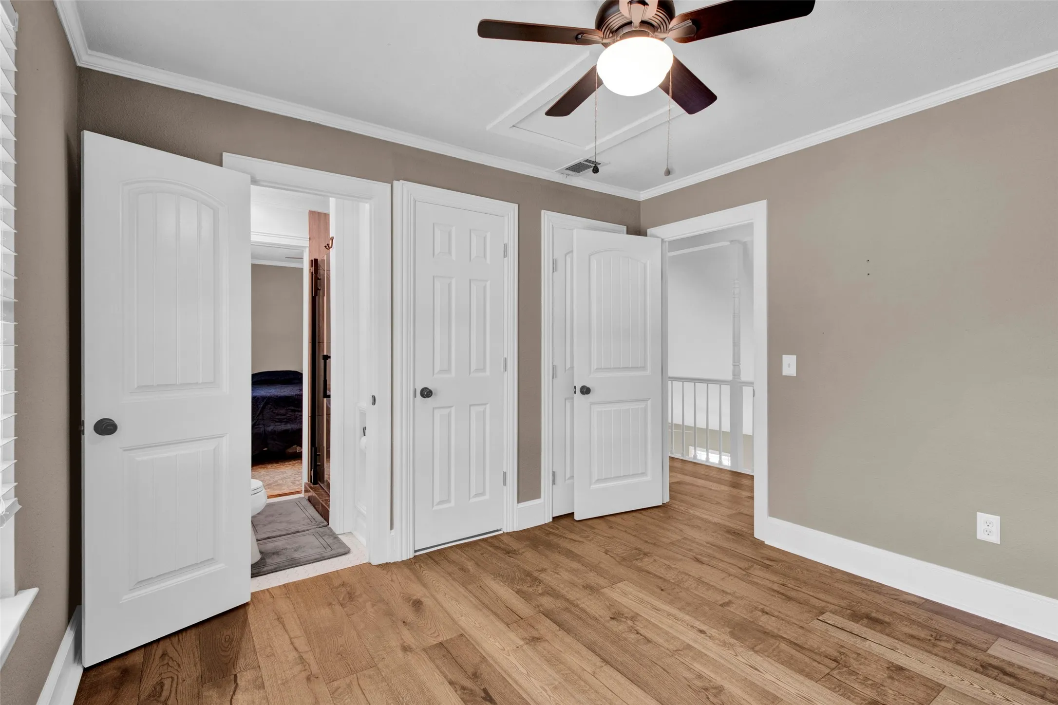 Wood-finish flooring, ceiling fan with integrated lighting, white trim, and multiple panel doors