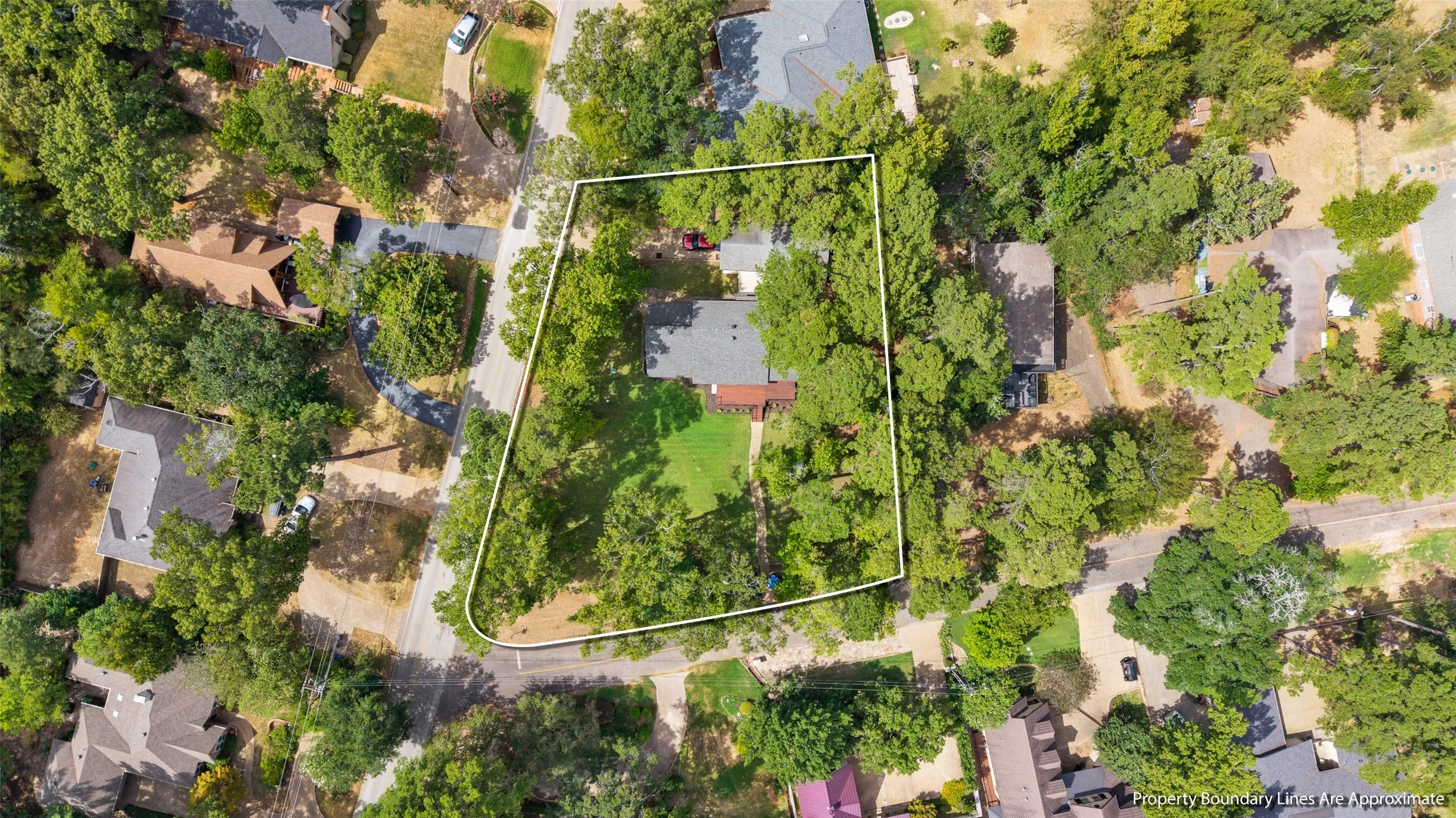 Property with mature trees, a manicured lawn, and an asphalt driveway, situated on a corner lot