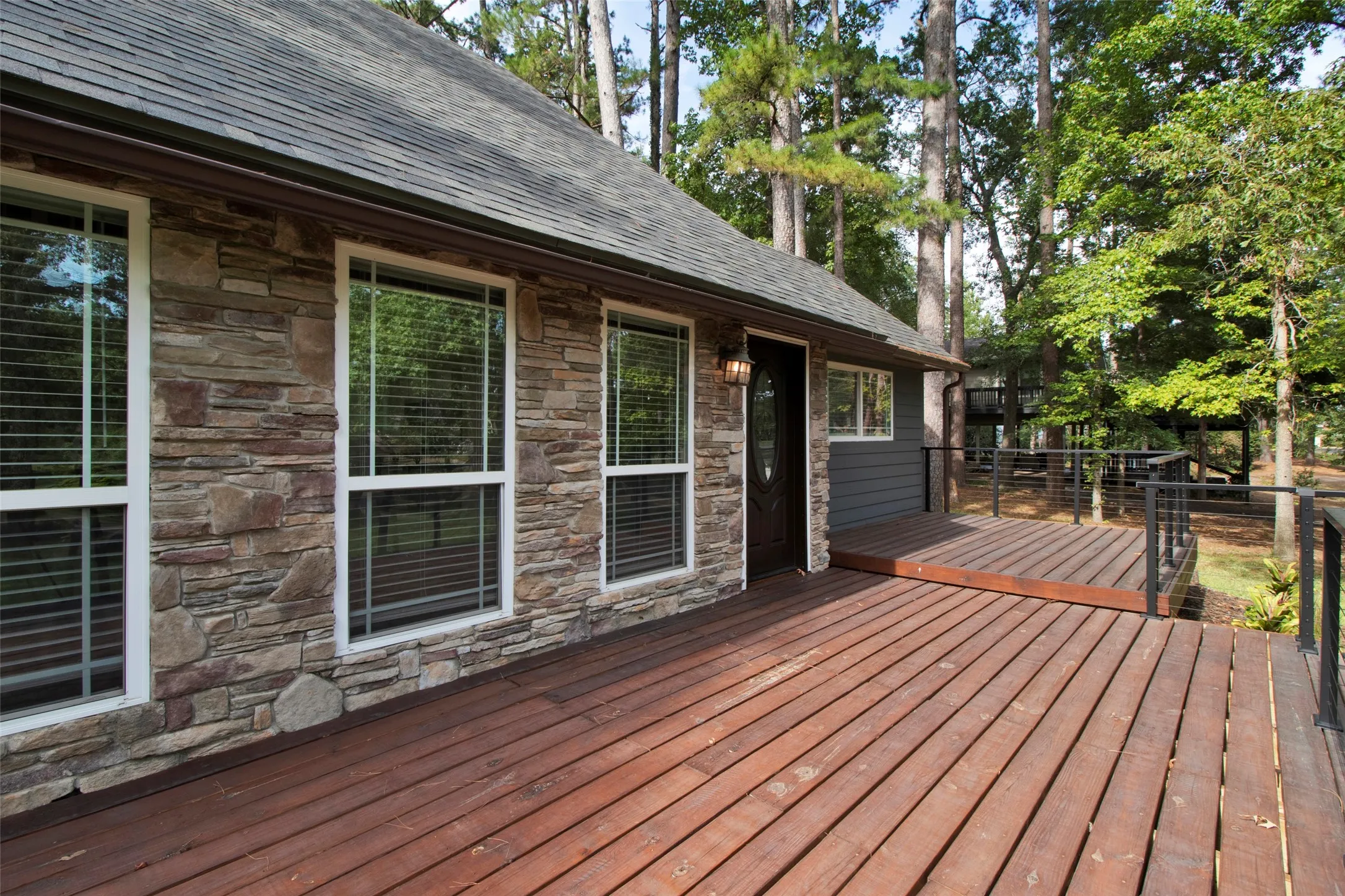 Stone facade with multiple windows, complemented by a wood deck featuring cable railings