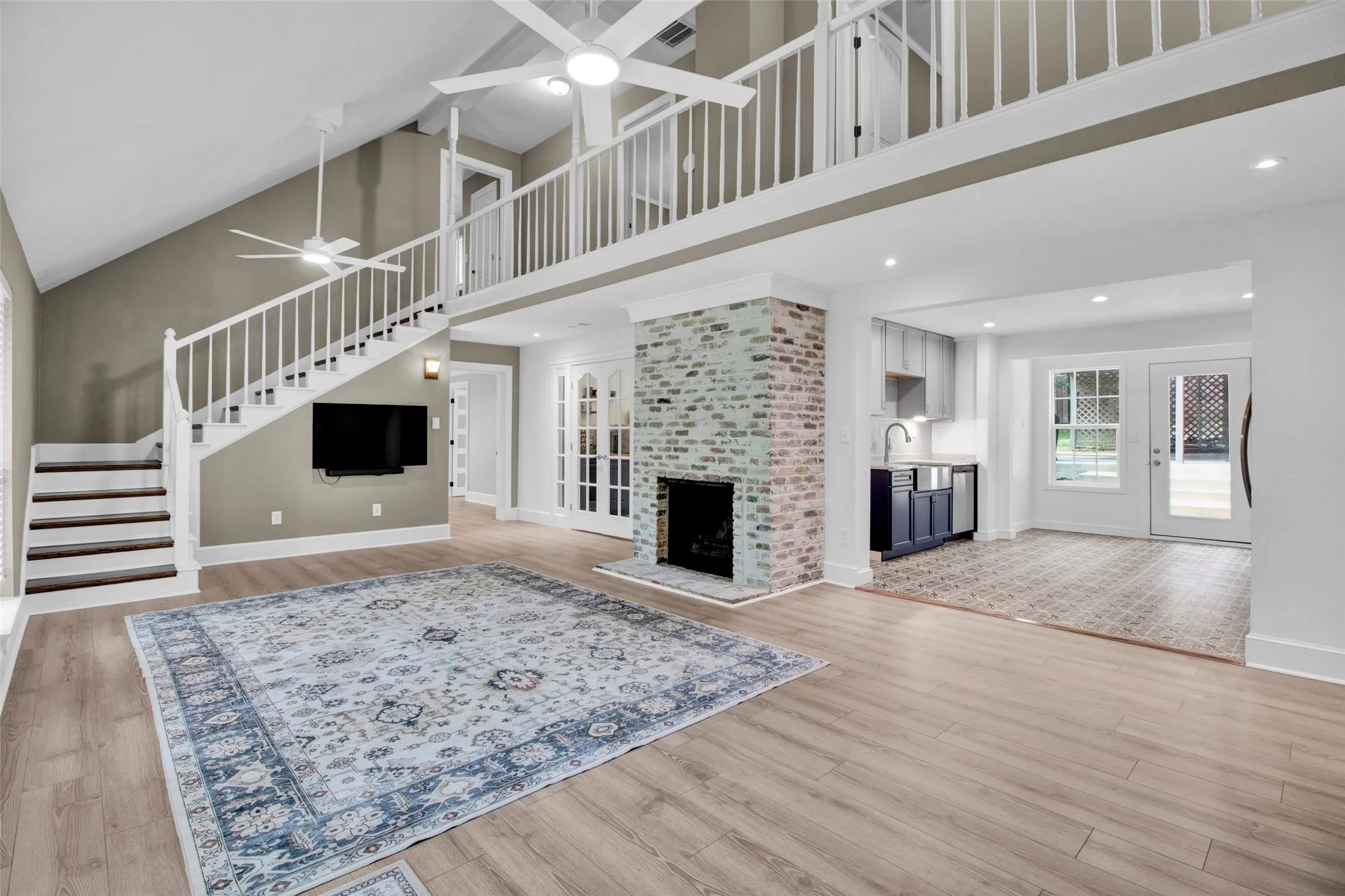 Vaulted ceilings with ceiling fans, light wood-finish flooring, white brick fireplace, wet bar with built-in cabinetry, and double French doors to the exterior