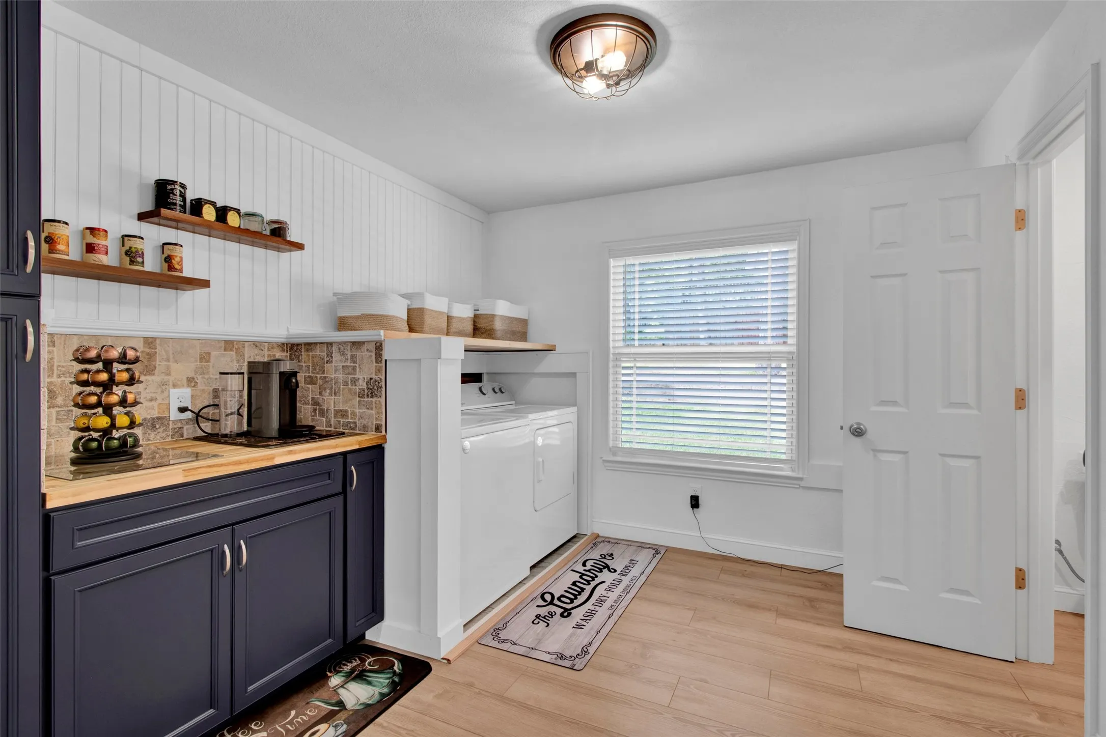 Wood-finish flooring, white beadboard accent wall, dark blue lower cabinetry, butcher block countertops, and a tiled backsplash