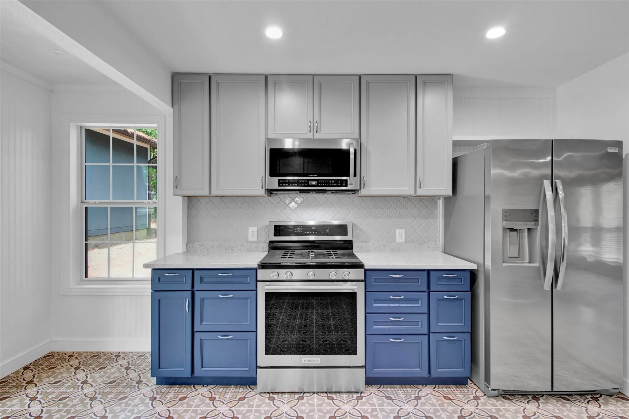 Modern kitchen with two-tone cabinetry, stainless steel appliances, patterned tile flooring, and a white tile backsplash