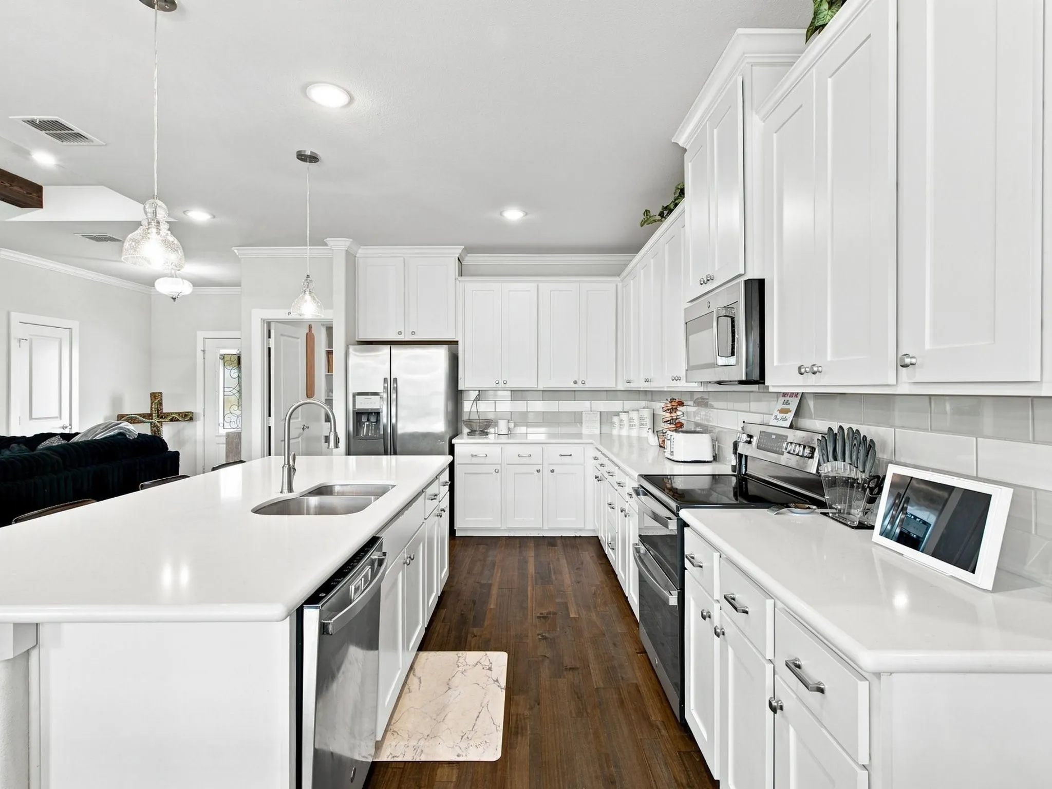 White cabinetry with crown molding, stainless steel appliances, wood-finish flooring, white countertops, and a subway tile backsplash