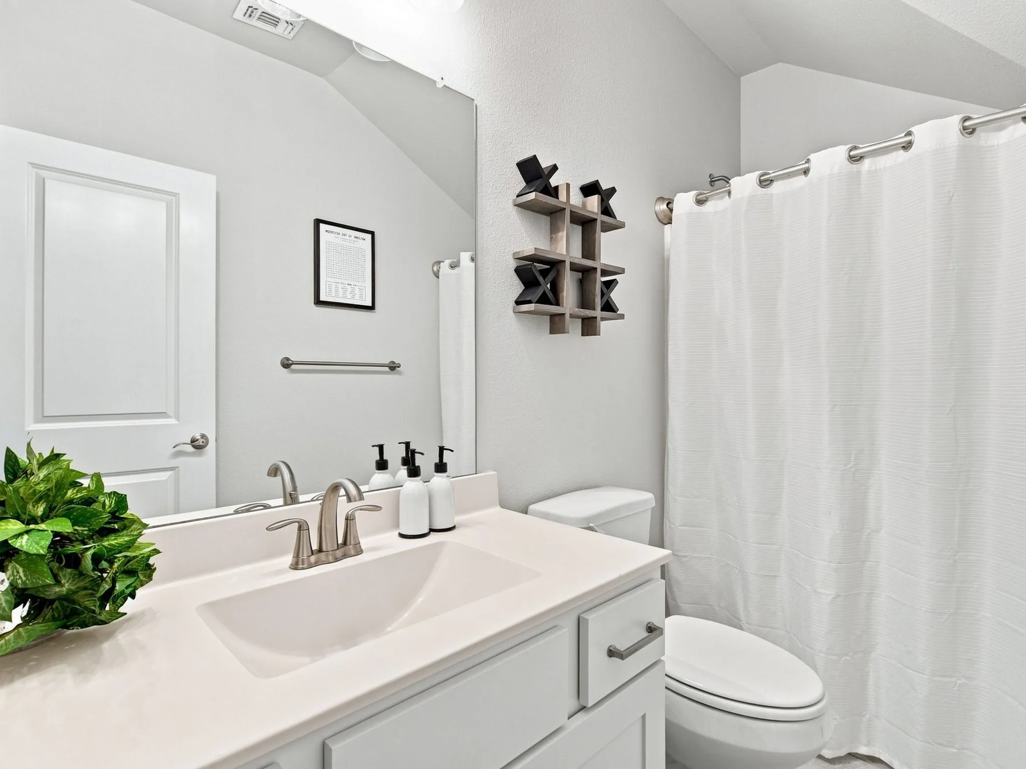 White vanity with an integrated sink and brushed nickel faucet, a wall-mounted mirror, and a toilet with a white shower curtain and rod - Second Floor Bathroom
