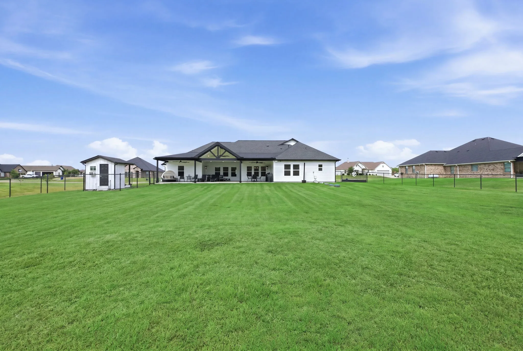 Expansive rear lawn, covered patio, white exterior siding, black roof, and a separate storage shed - Virtual Grass