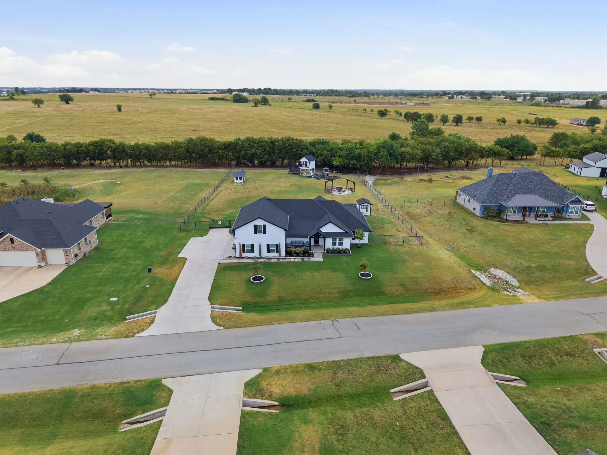 White exterior with dark roof, concrete driveway, fenced yard, and expansive green lawn
