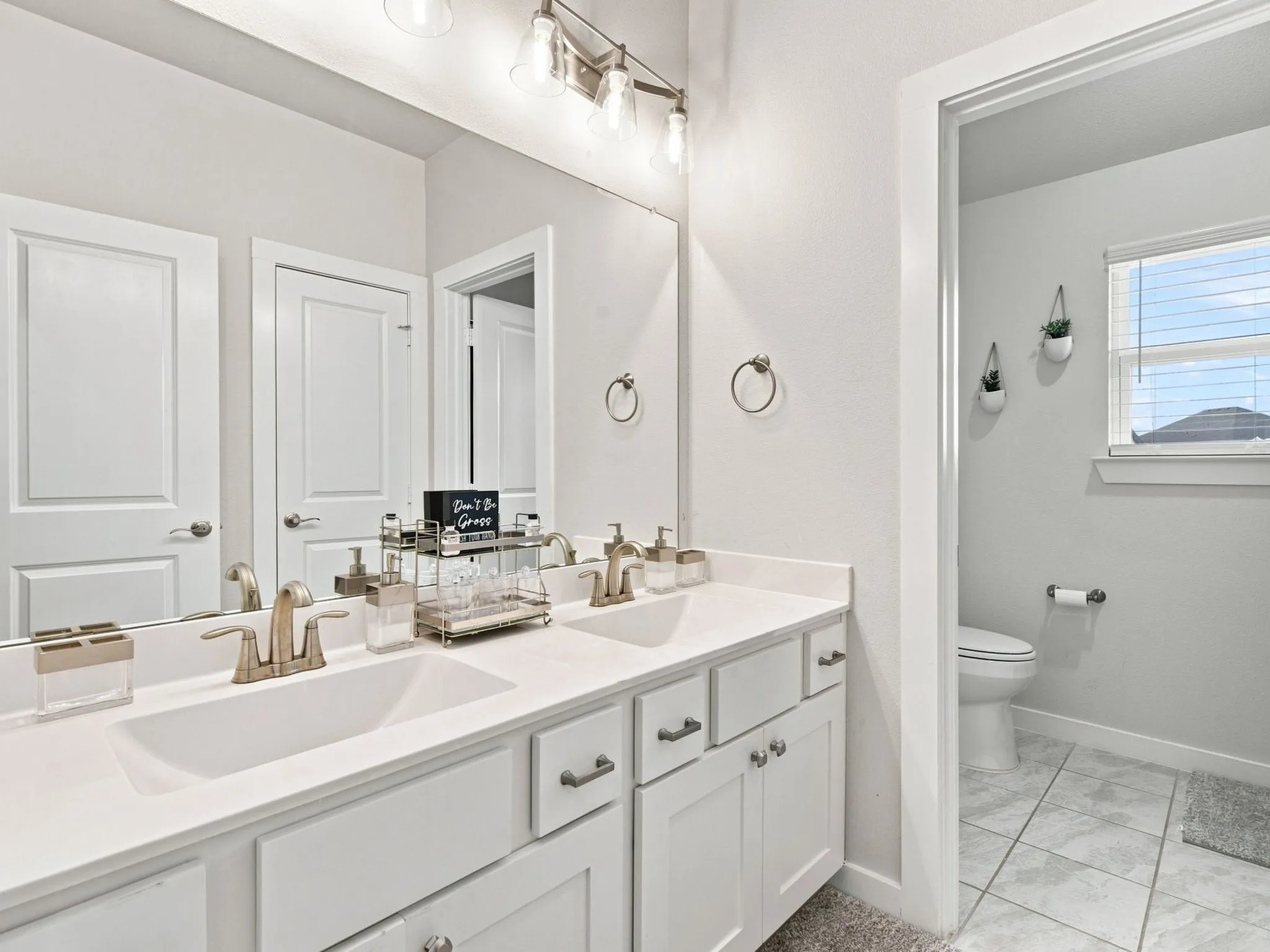 Dual basin vanity with brushed nickel fixtures and white cabinetry, complemented by a large wall-mounted mirror and overhead lighting