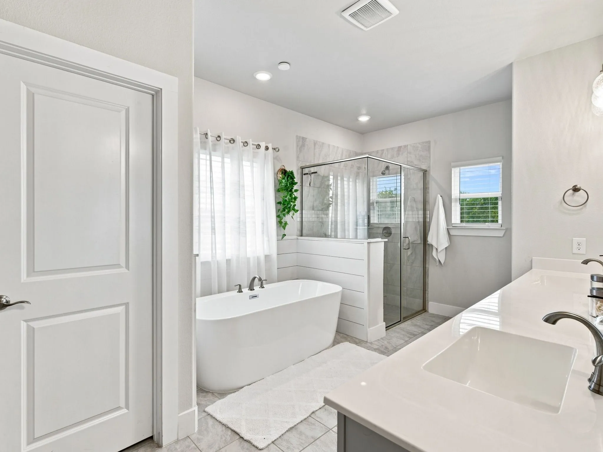 Freestanding soaking tub, glass-enclosed shower with tile surround, dual vanity with undermount sinks, and windows providing natural light