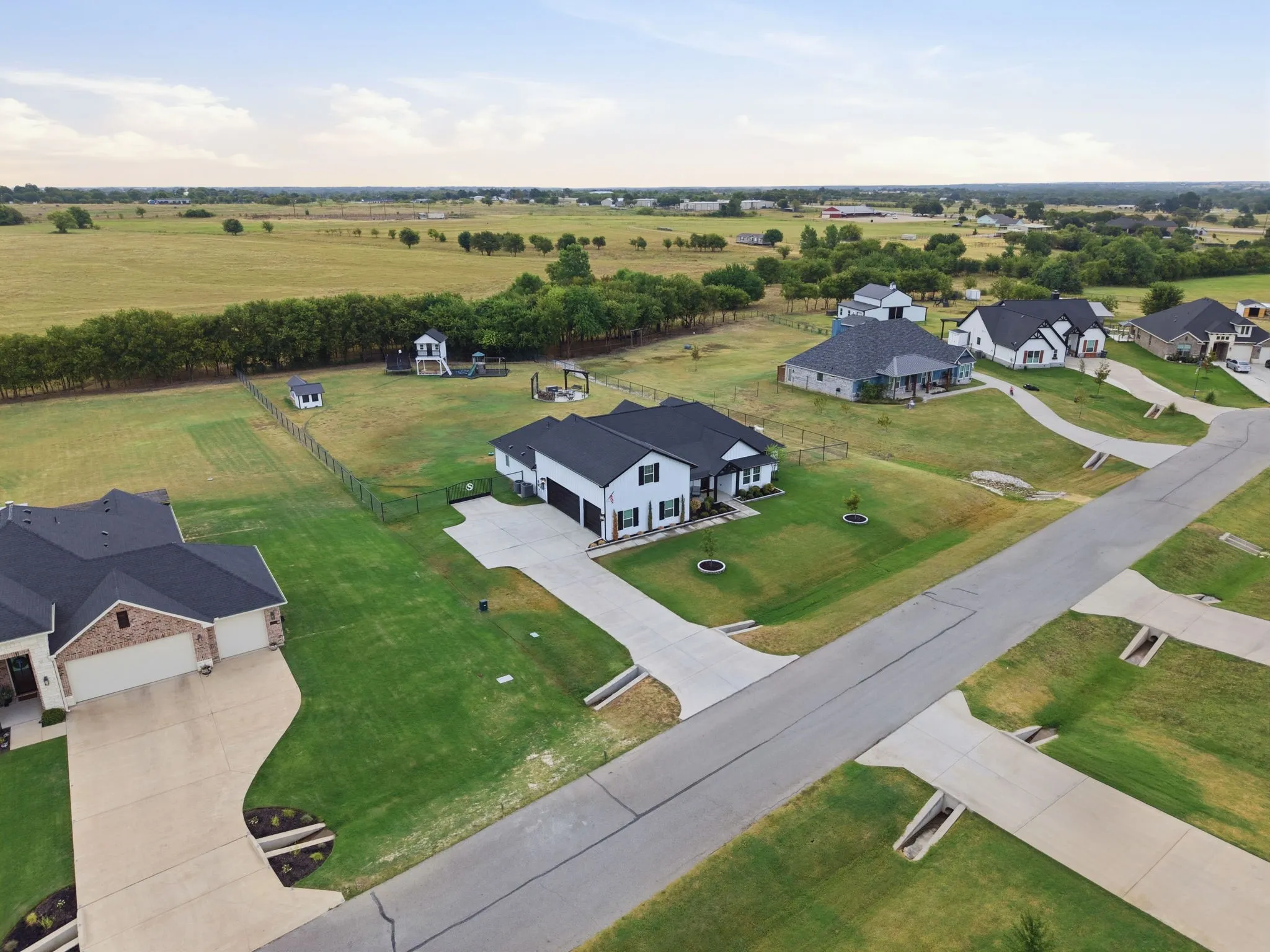 Expansive property featuring a concrete driveway, manicured lawn, and perimeter fencing