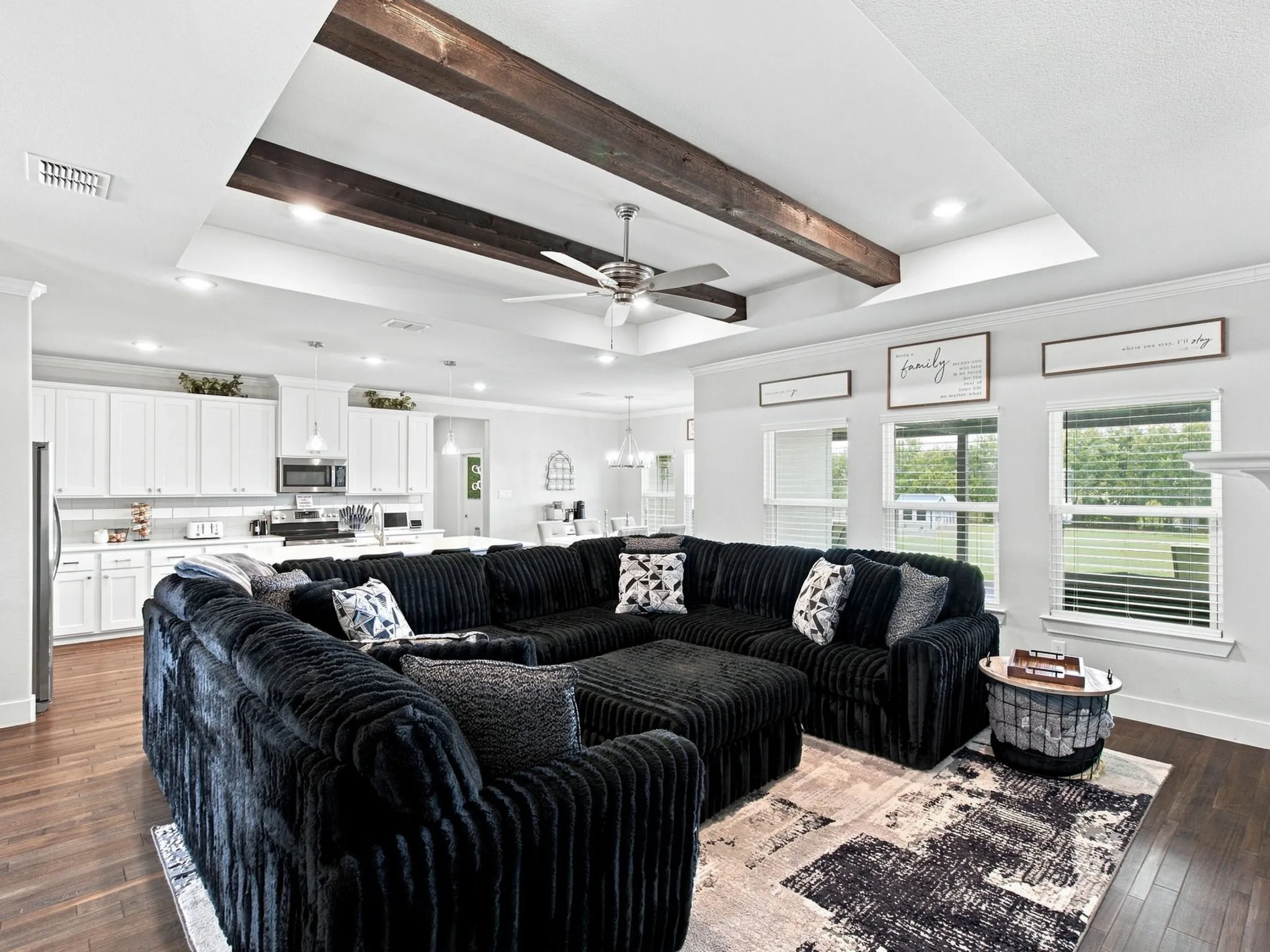 Tray ceiling with exposed wood beams, recessed lighting, ceiling fan, wood-finish flooring, and white kitchen cabinetry
