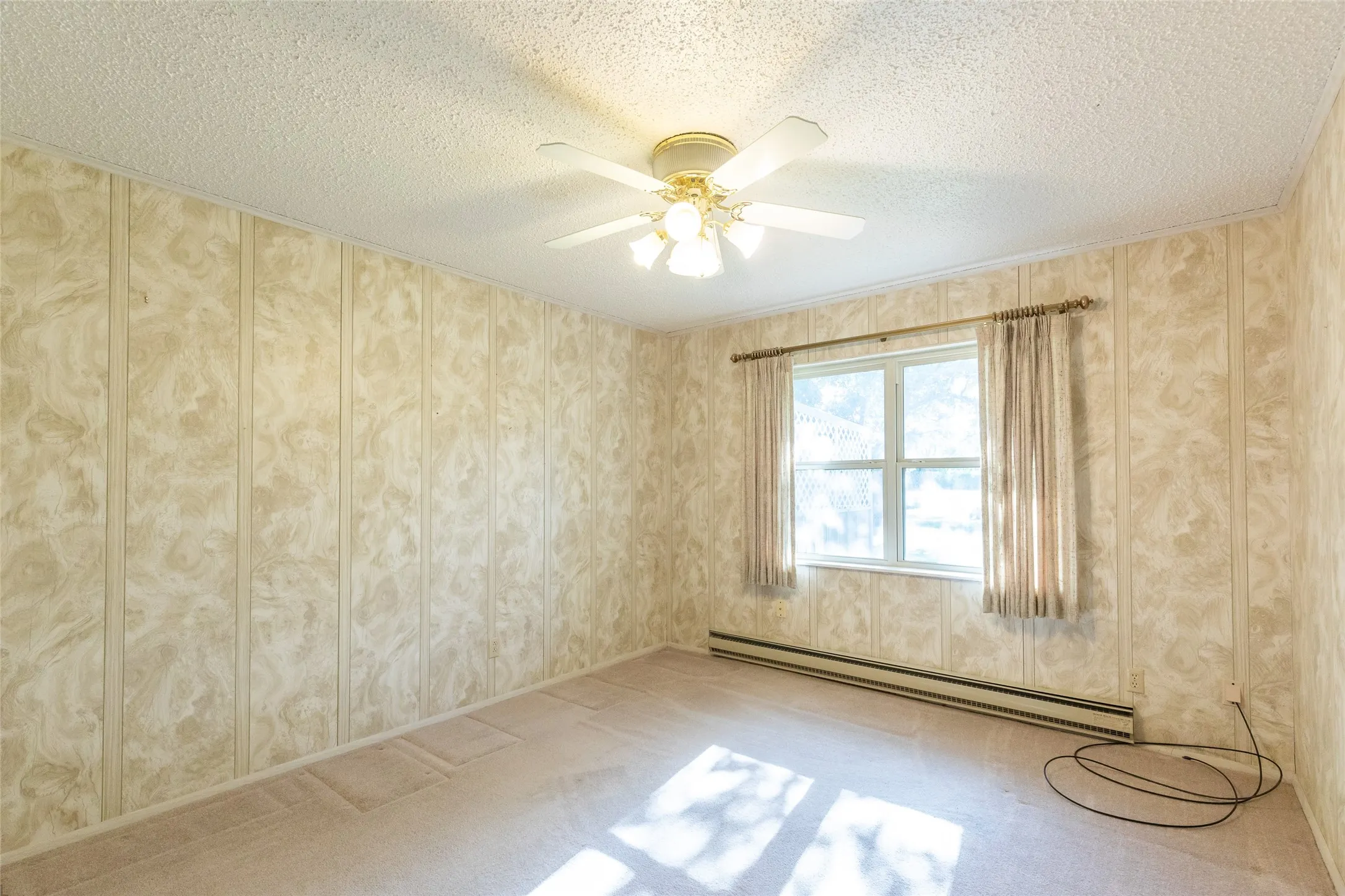 Ceiling fan with integrated lighting, textured ceiling, panel-style wall covering, large window, and carpeted flooring