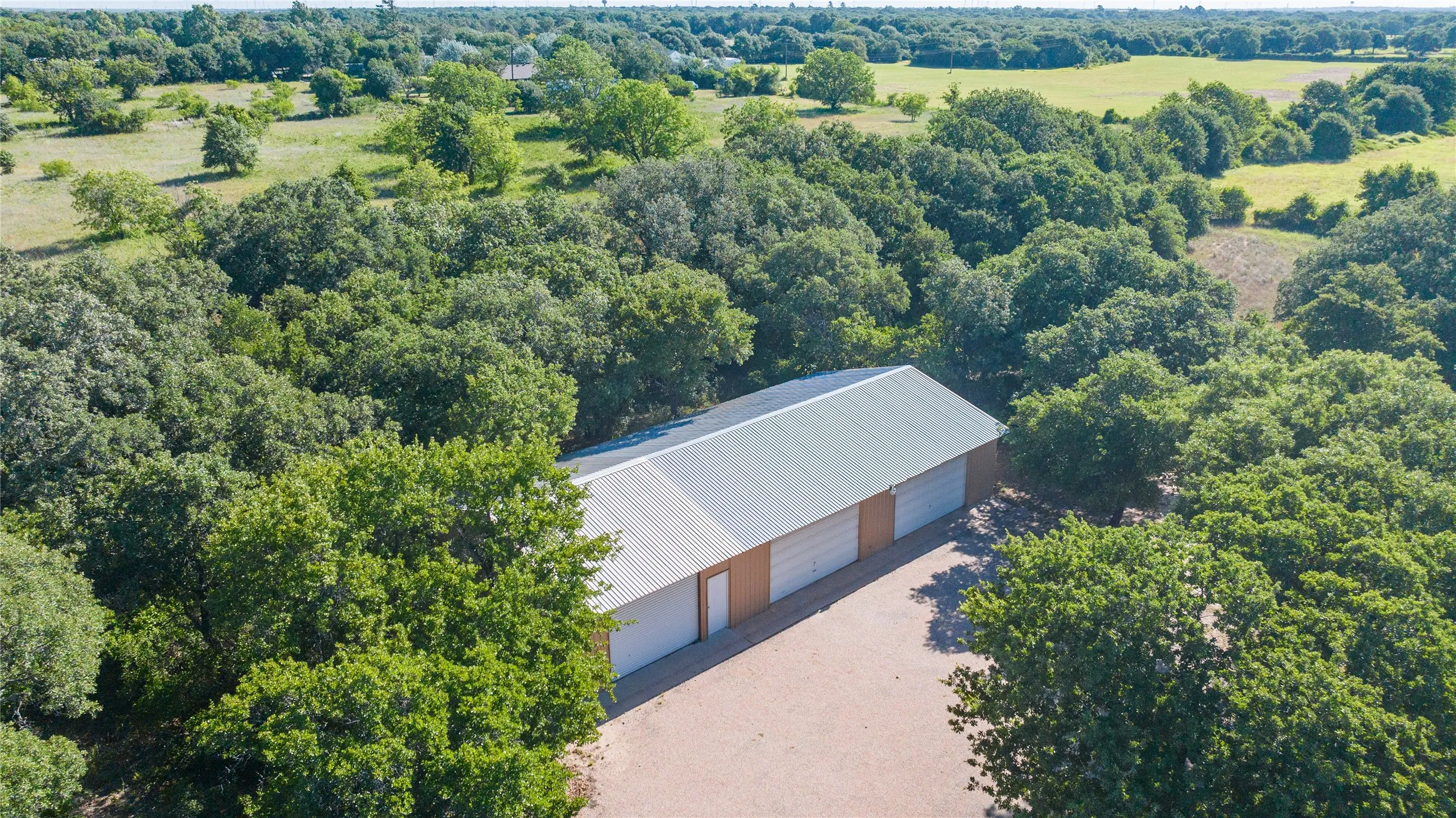 Outbuilding with a metal roof, three garage doors, and a gravel driveway