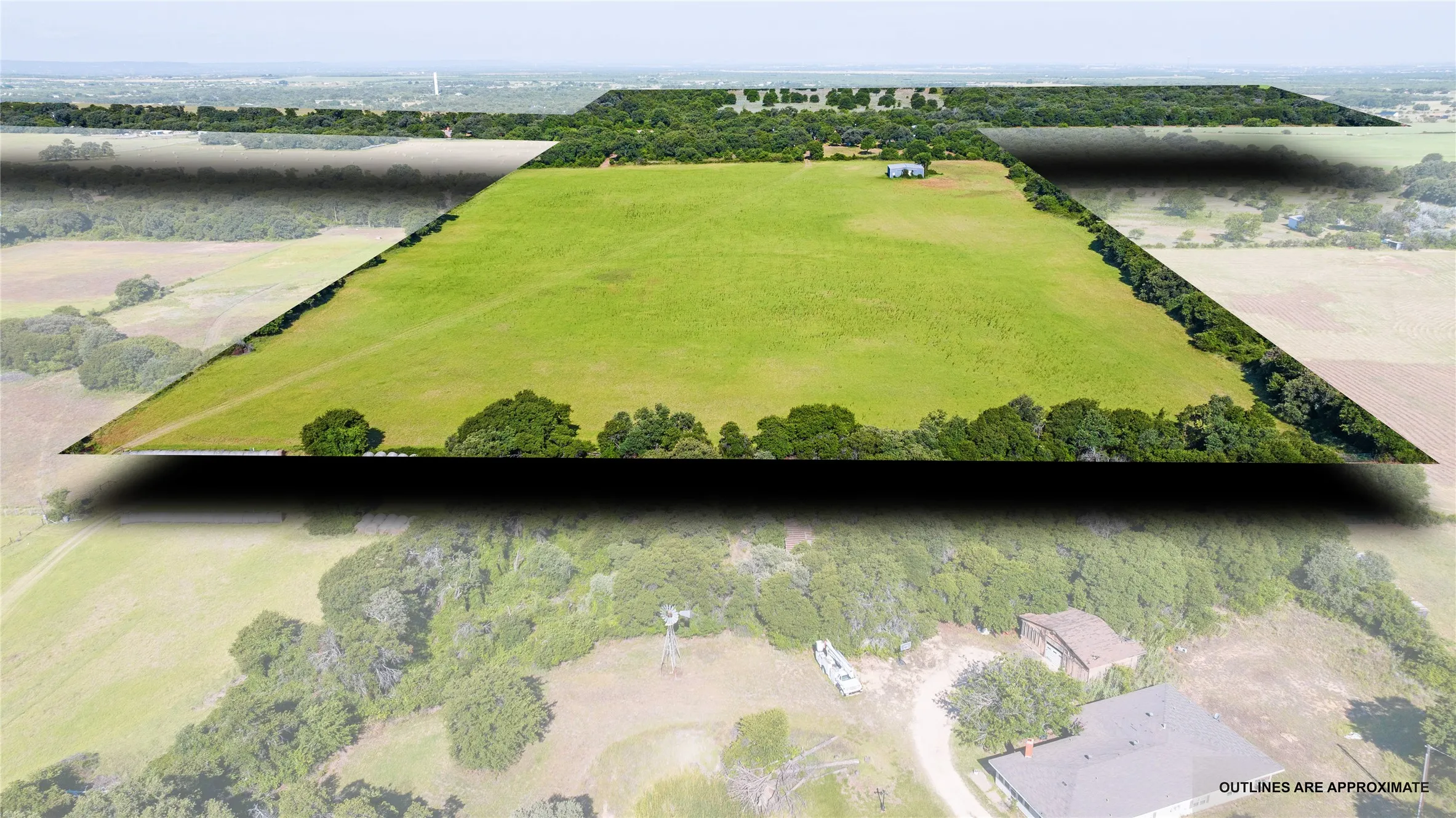 Expansive land parcel featuring a green field, natural tree lines, and a visible building structure