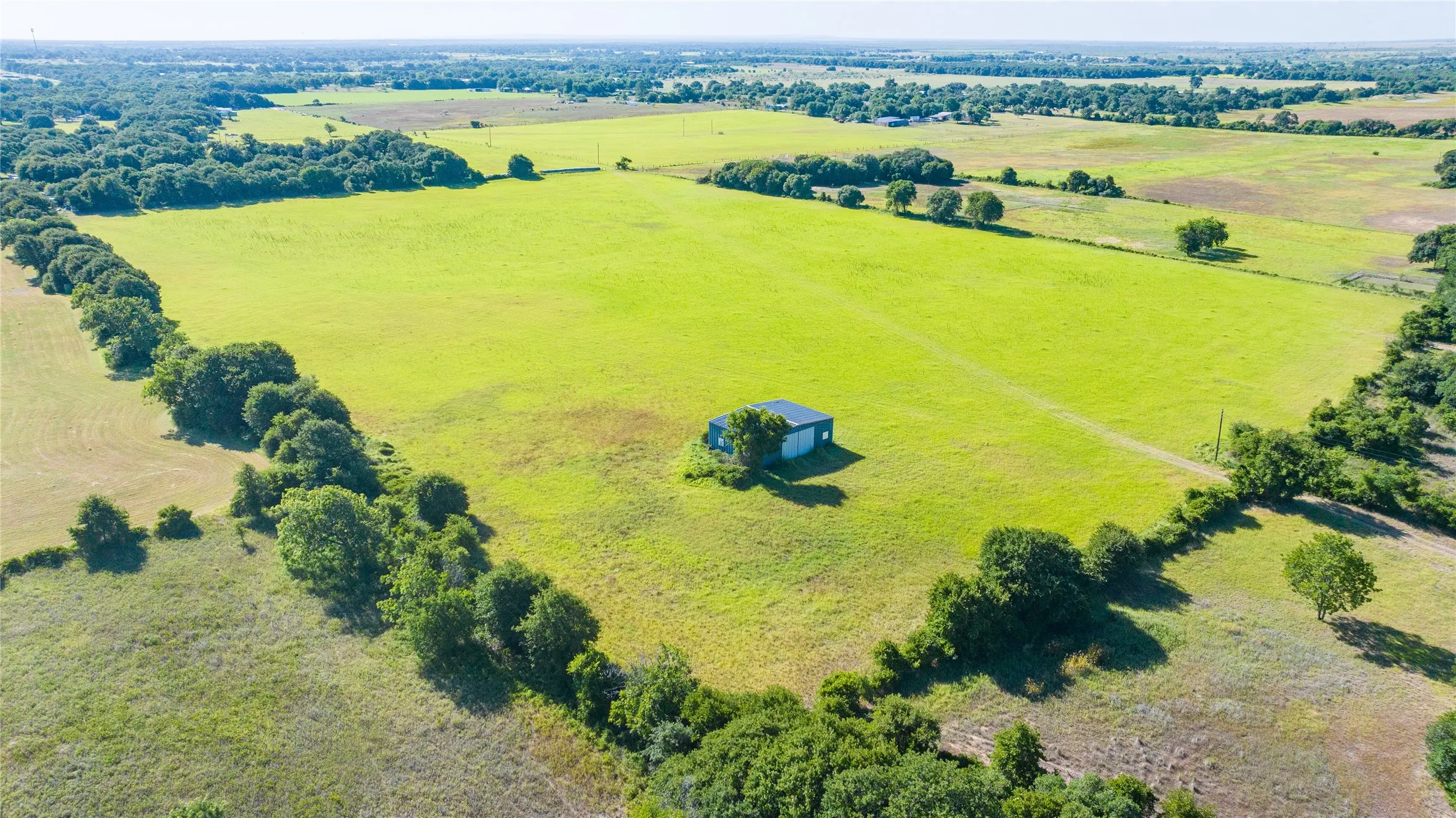 Expansive green fields with mature tree lines and a standalone structure