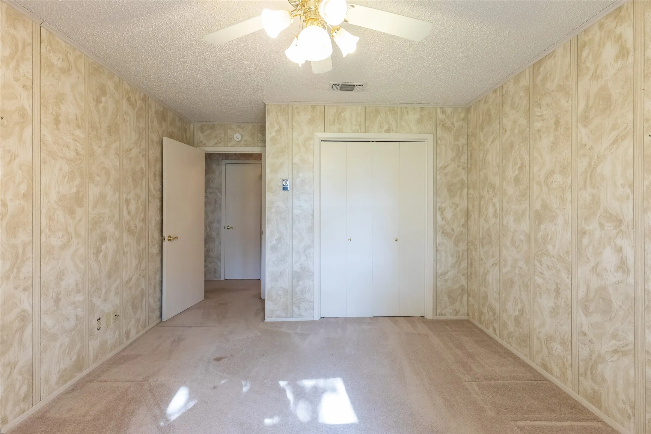 Carpeted flooring with paneled walls, ceiling fan with integrated lighting, and bi-fold closet doors