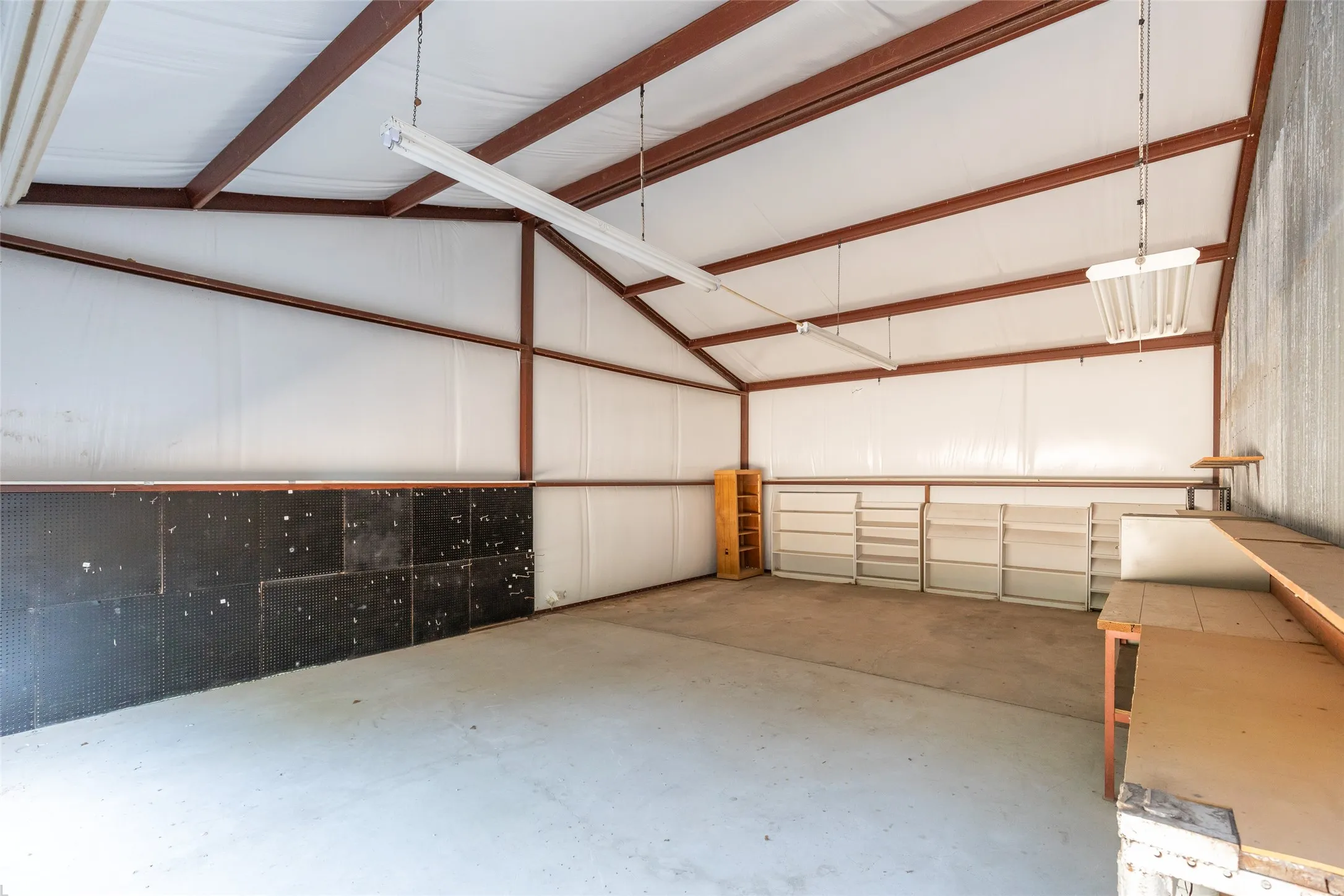 Spacious interior with exposed metal beams, concrete flooring, and ample overhead lighting