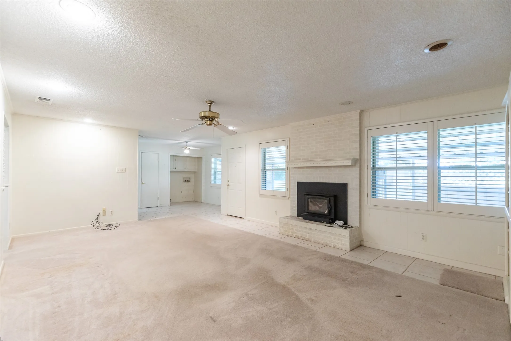 Carpeted living area with a white painted brick fireplace, a built-in wood stove, and a ceiling fan