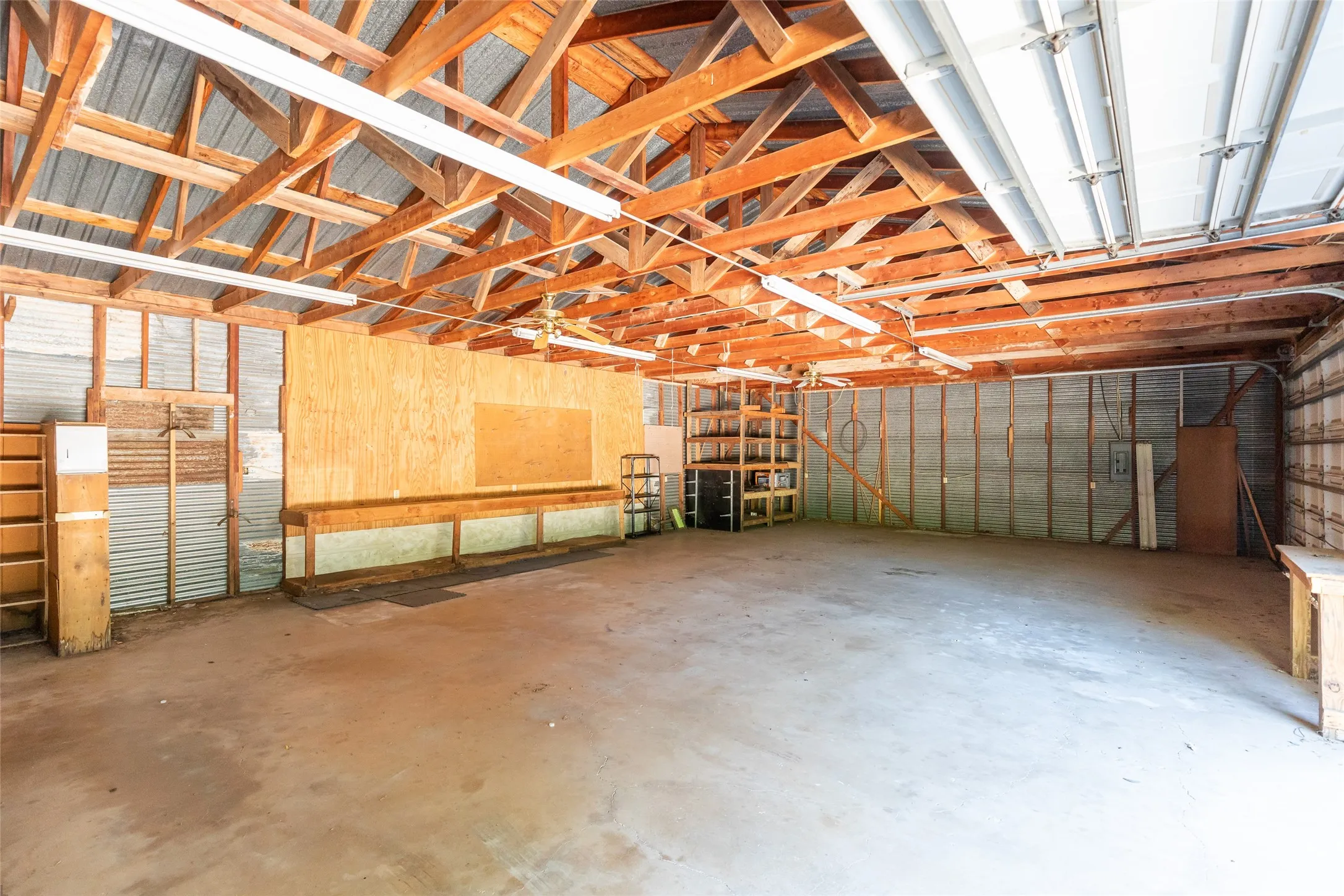 Spacious garage with exposed wood beam ceiling, concrete flooring, and ample fluorescent lighting