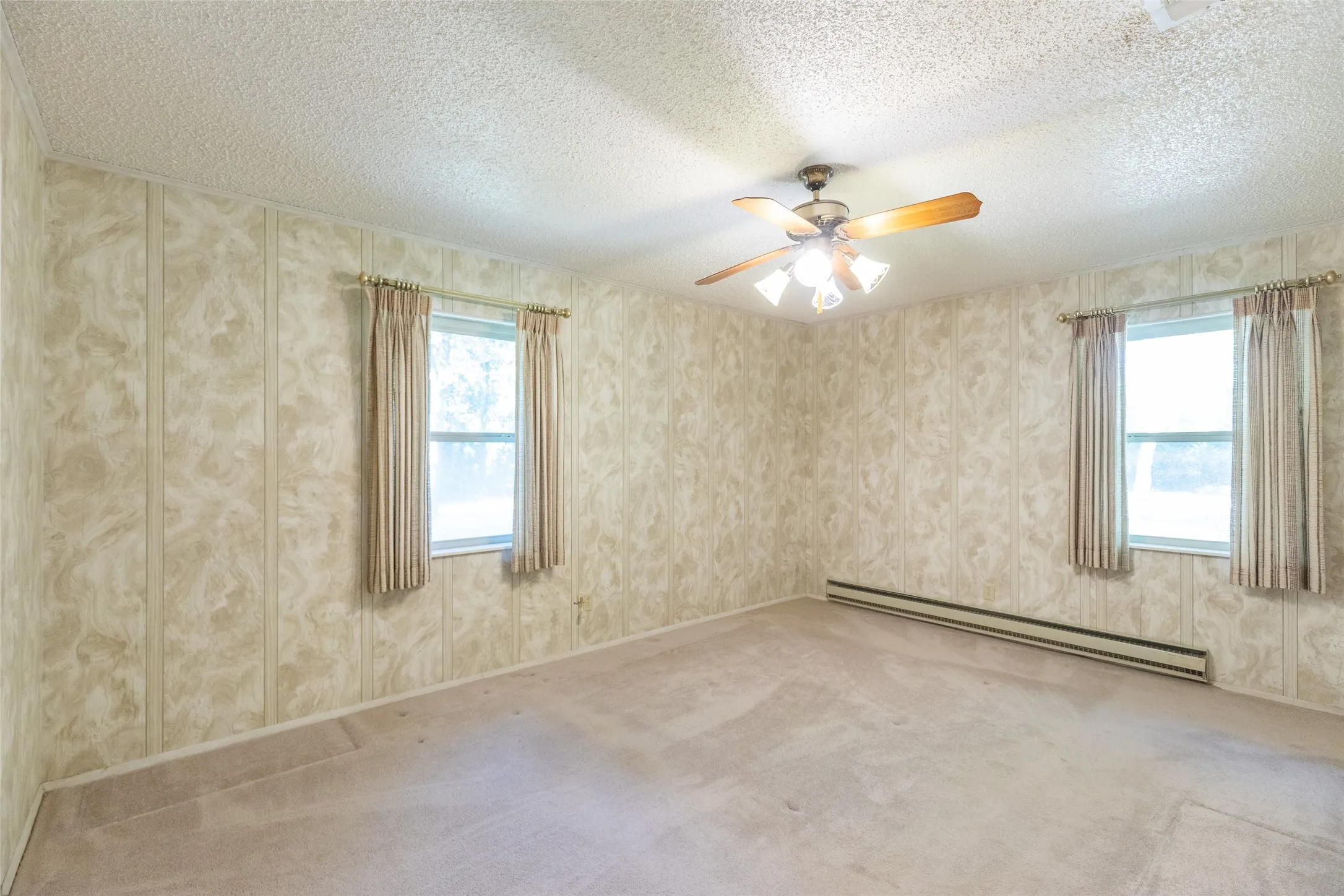 Paneling walls, textured ceiling, two windows, wall-mounted heating unit, and a ceiling fan with light fixture