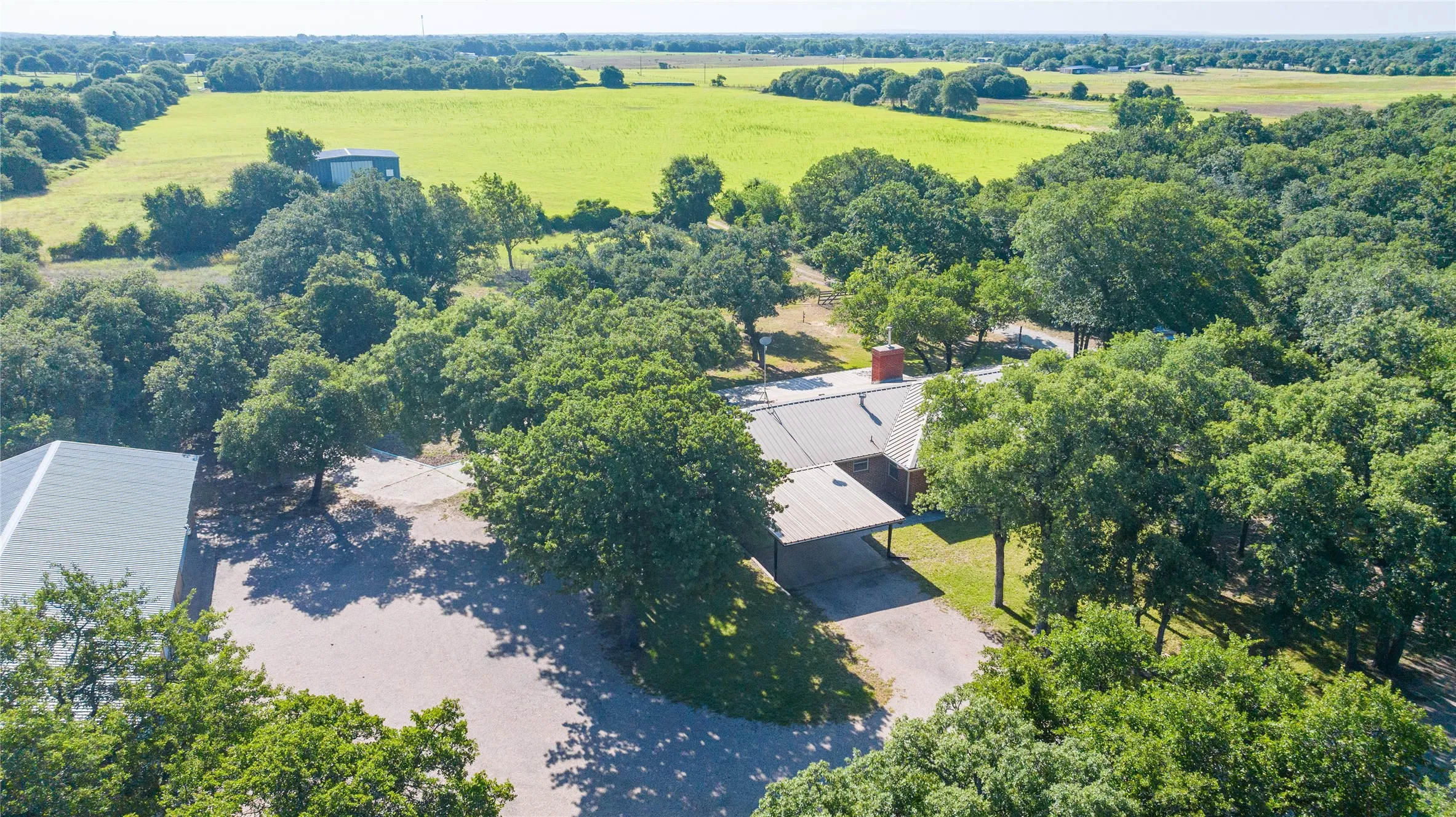 Expansive property featuring a mature tree canopy, a large outbuilding with a metal roof, and a gravel driveway