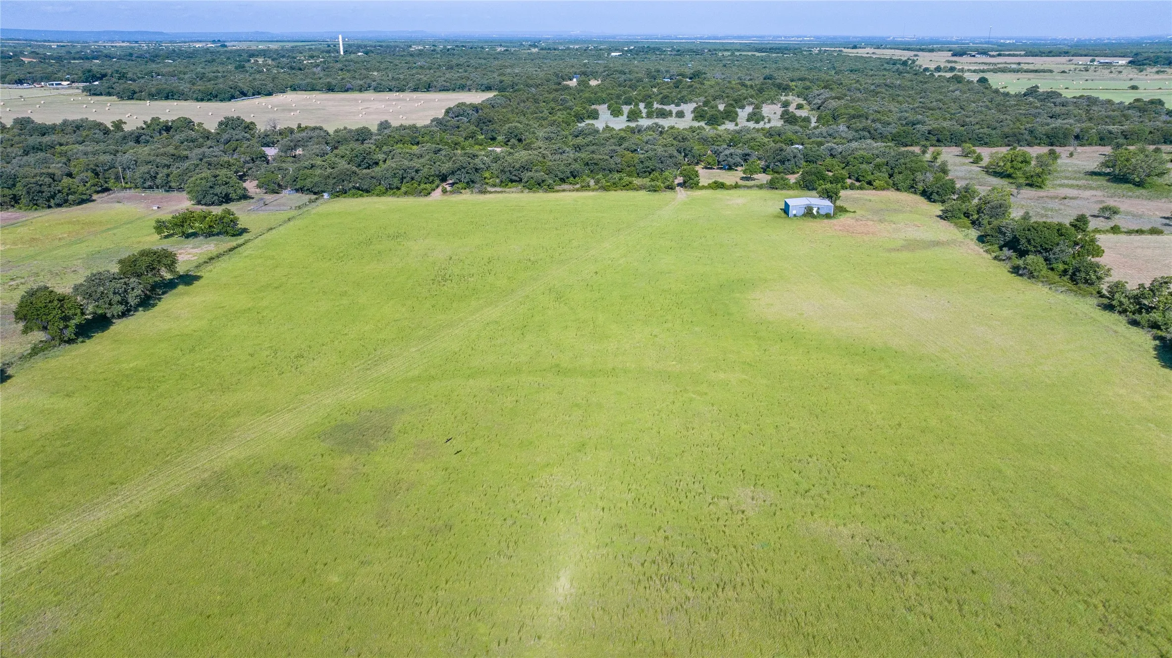 Expansive green pasture with a metal utility building and surrounding mature trees