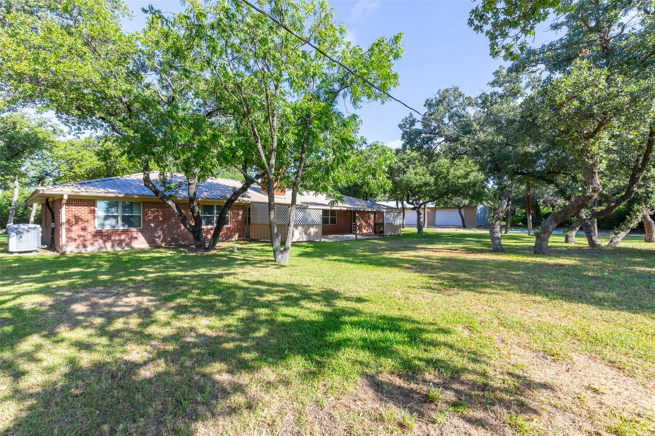 Brick facade residence with a metal roof and mature trees on a grassy lot
