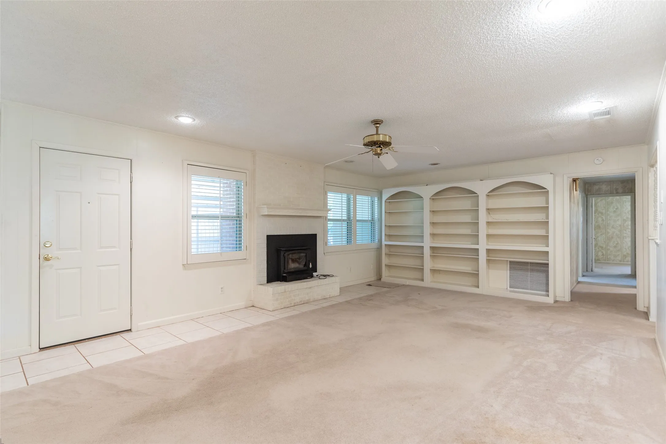 Spacious room featuring a brick fireplace, built-in shelving, windows with blinds, and a ceiling fan
