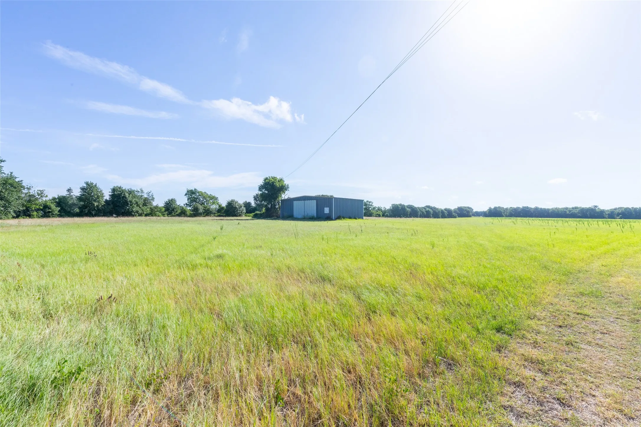 Expansive open land with a metal outbuilding and distant tree line