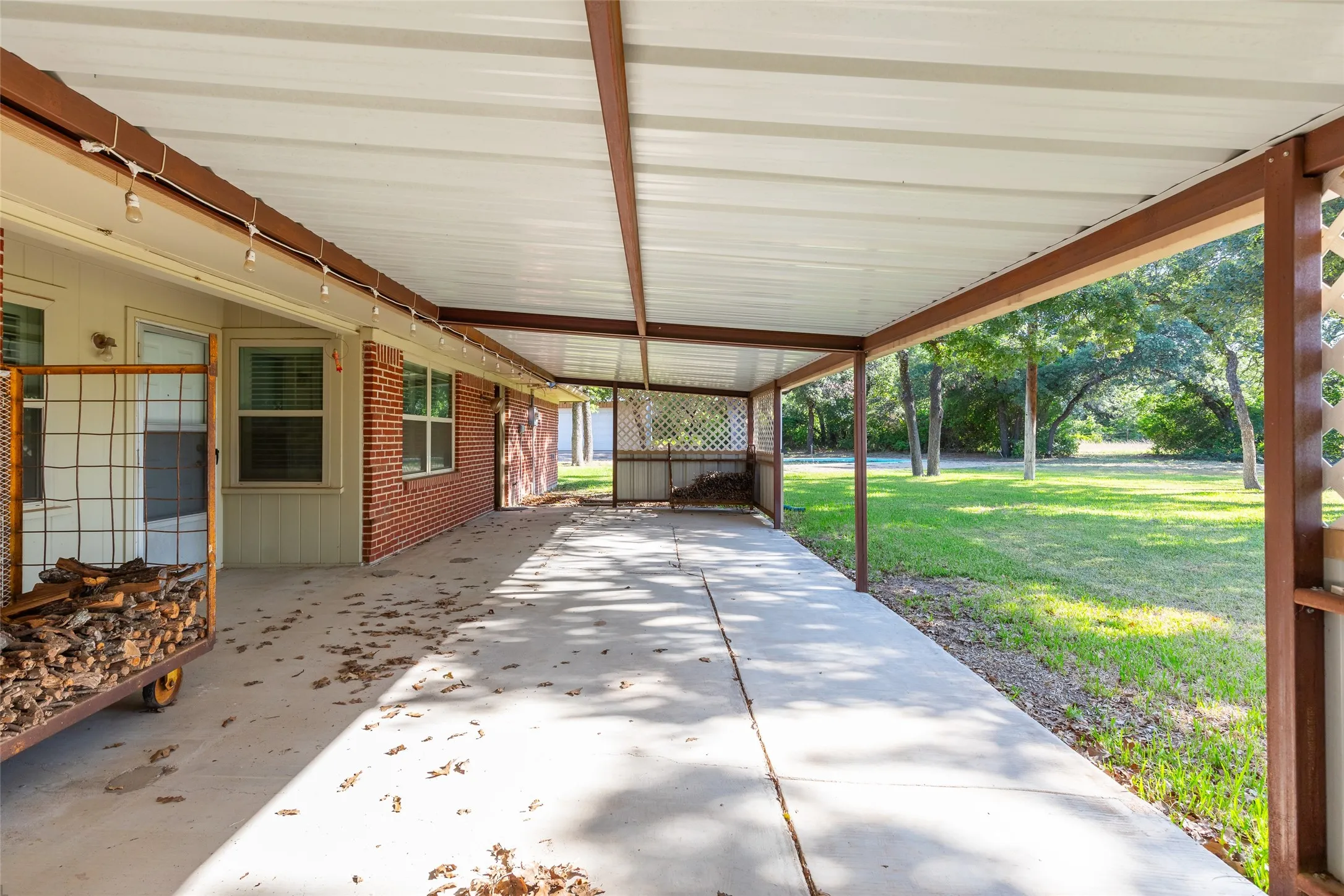Expansive covered patio with a concrete surface, metal support beams, and a white corrugated roof