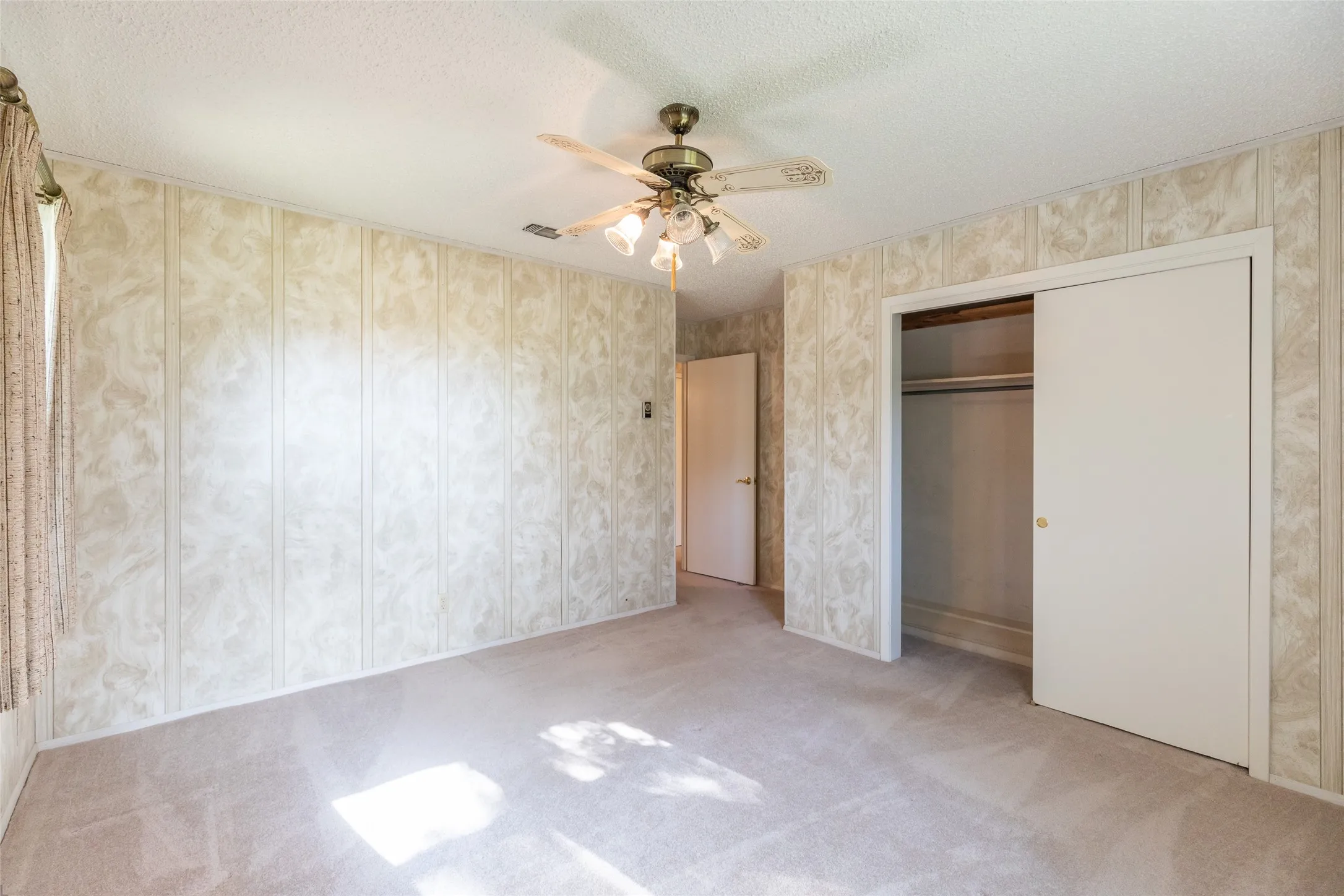 Textured wall paneling, light-colored carpeting, a ceiling fan with integrated lighting, and a bi-fold closet with shelving and hanging rod
