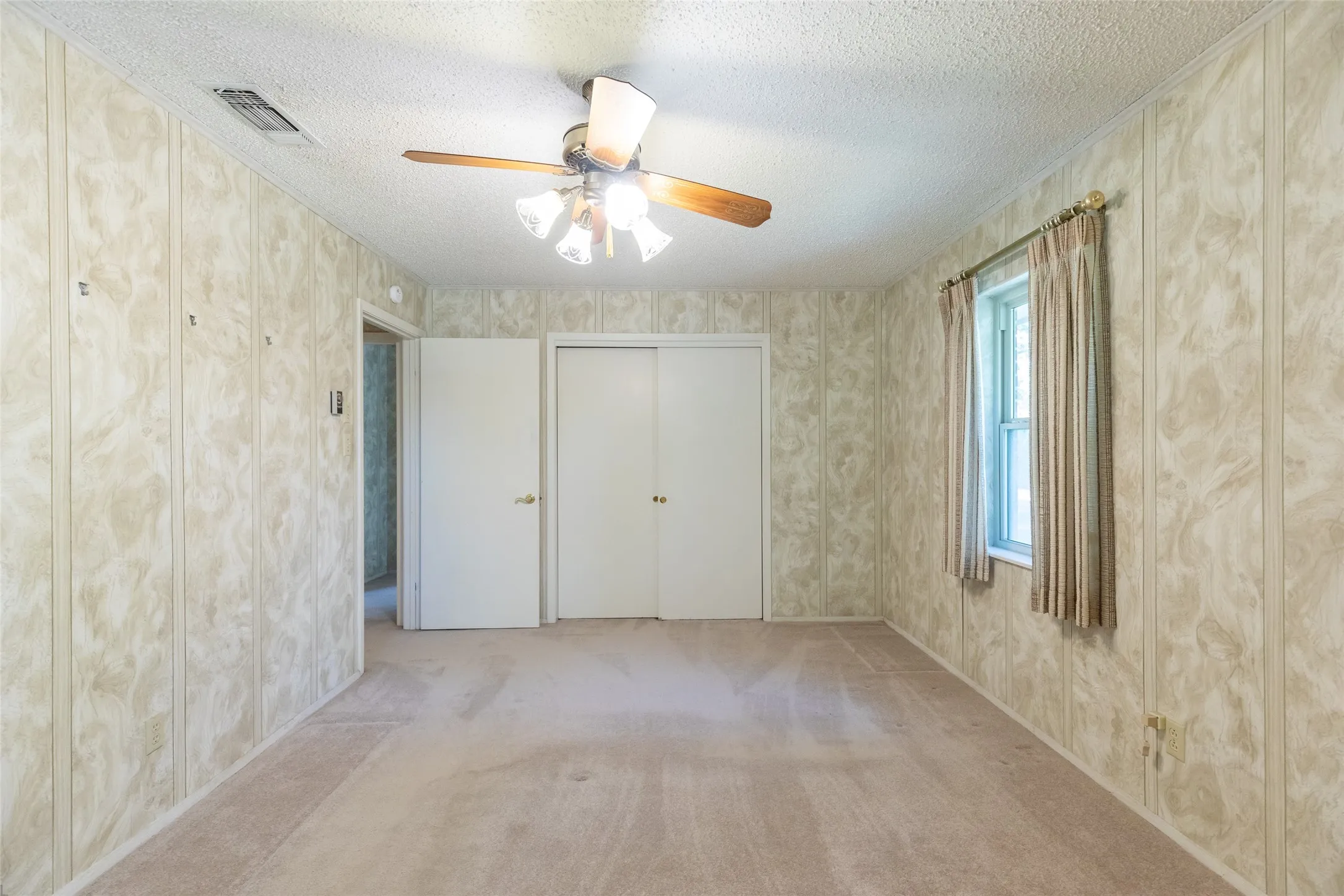 Recessed window with drapes, paneled walls, ceiling fan with light fixture, and carpet flooring