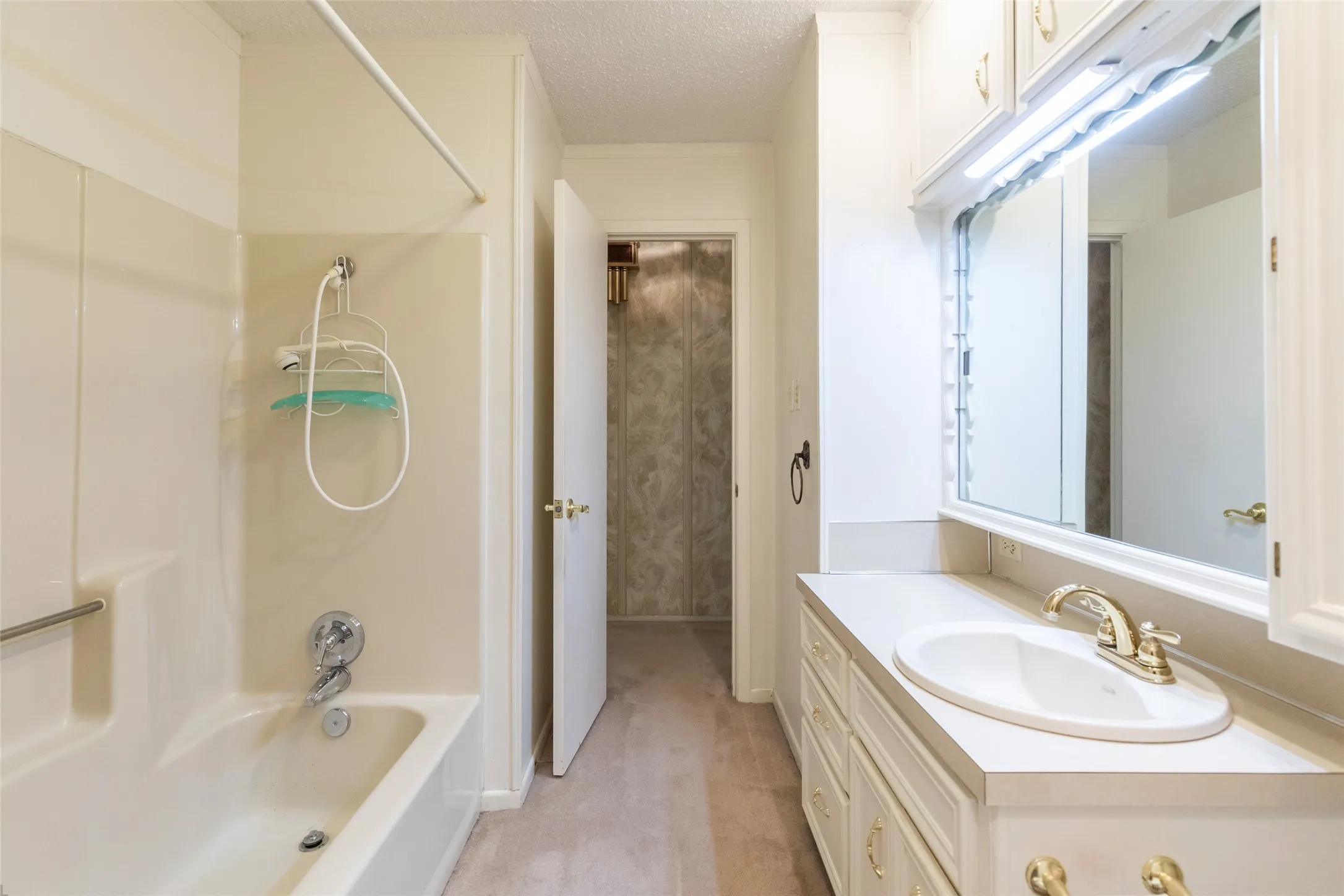 Spacious bathroom featuring a white vanity with integrated sink, gold-tone fixtures, and a large mirror with overhead lighting