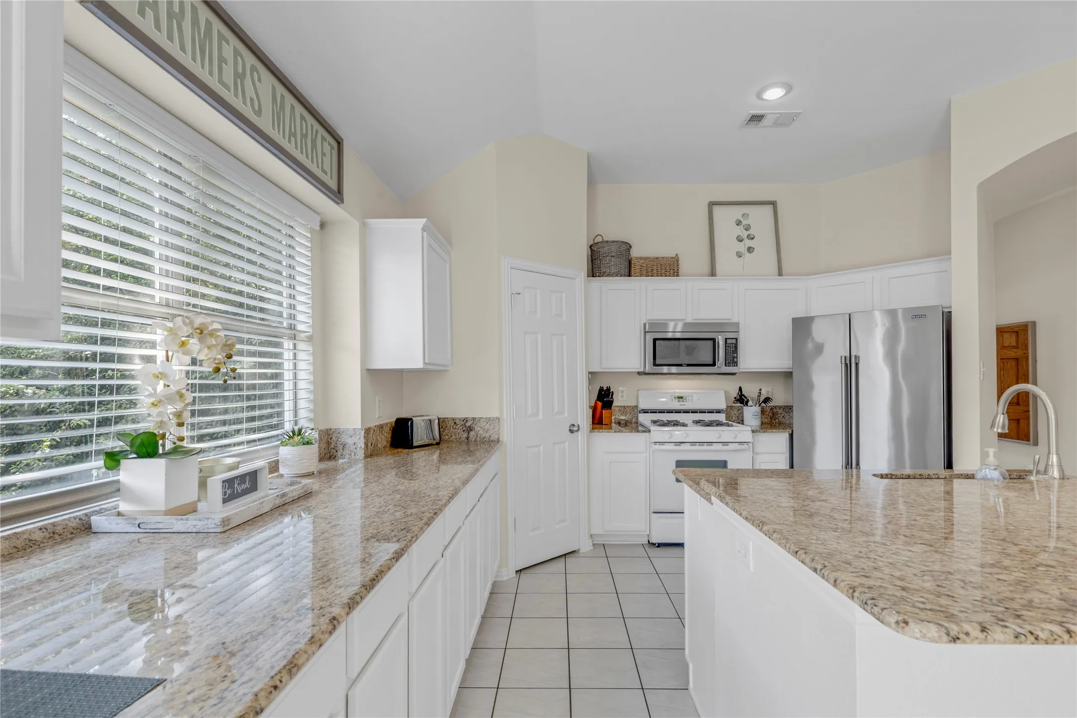 Kitchen featuring extensive countertop space, white cabinetry, integrated stainless steel appliances, and tile flooring