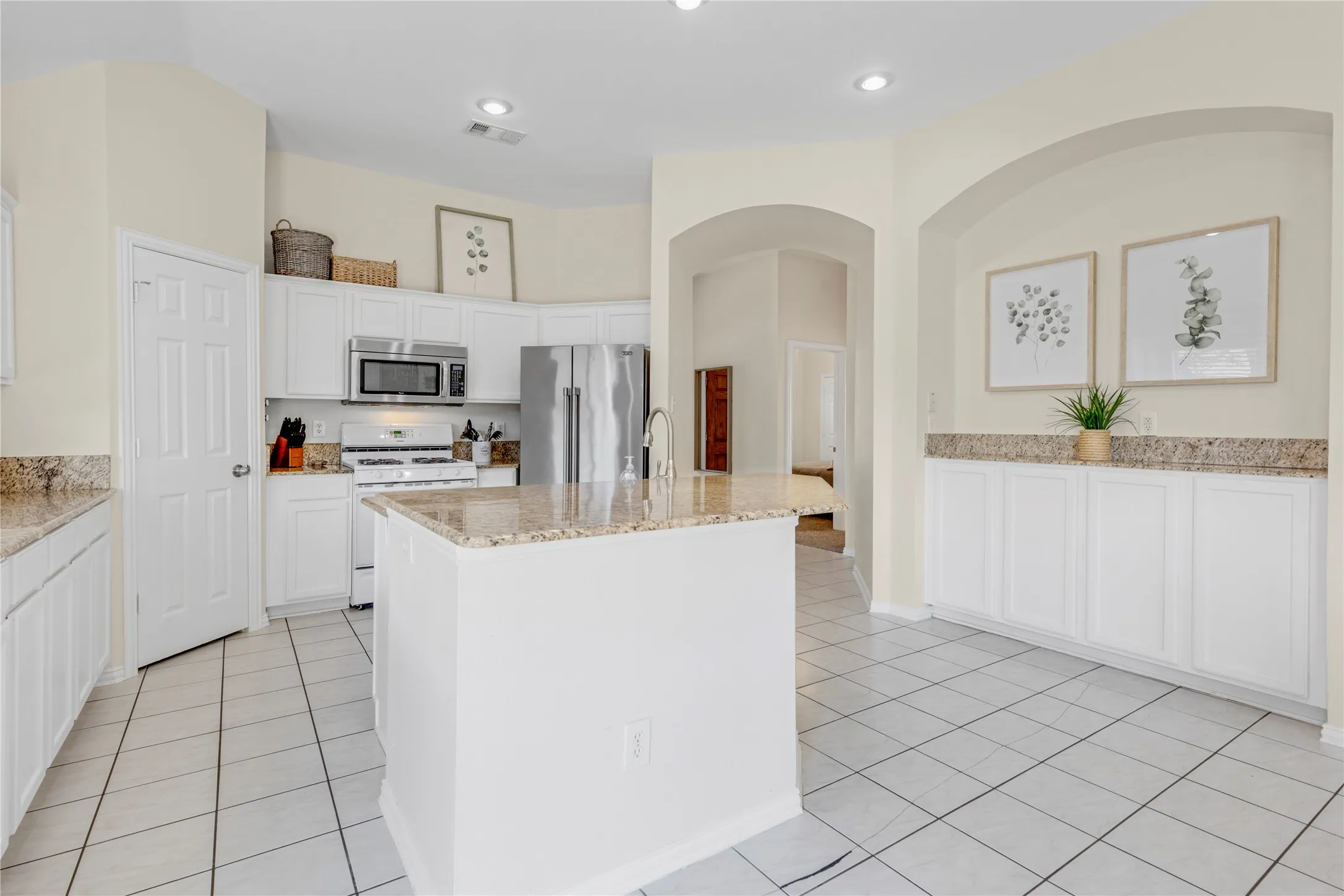 Kitchen with white cabinetry, granite countertops, stainless steel appliances, a central island, and tile flooring