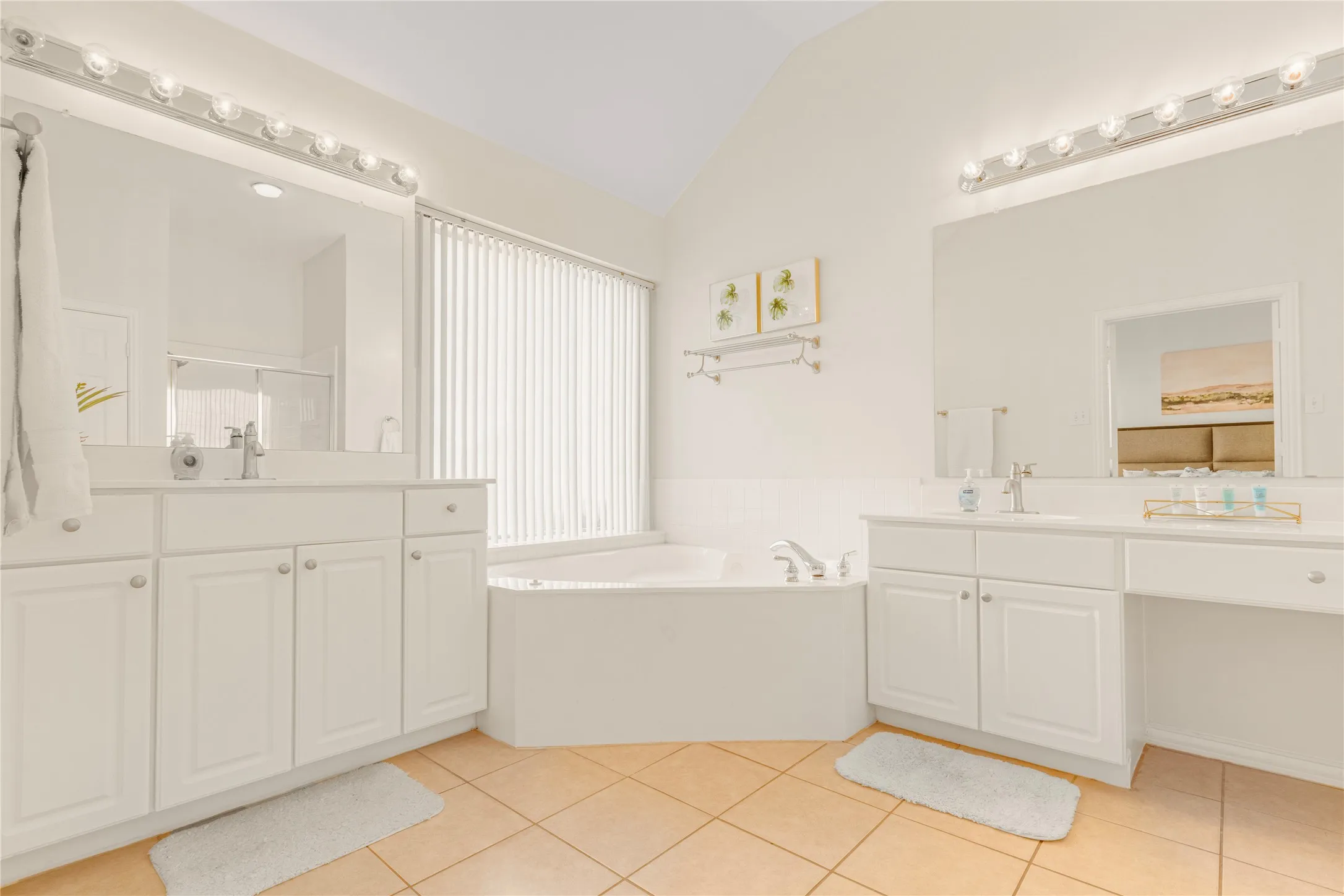 Dual vanity with white cabinetry, built-in soaking tub, large window with vertical blinds, and tile flooring