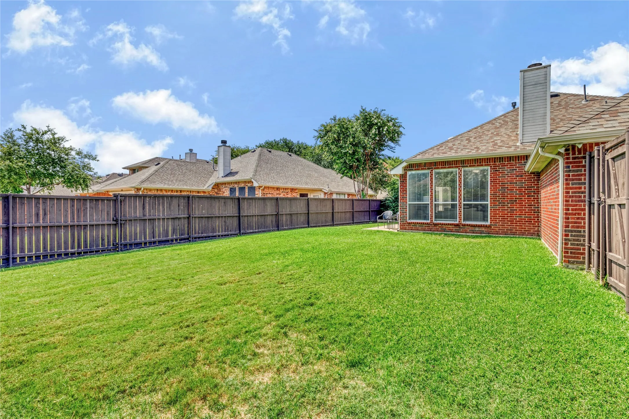 Expansive backyard featuring a manicured lawn, full privacy fencing, and brick exterior with multiple windows