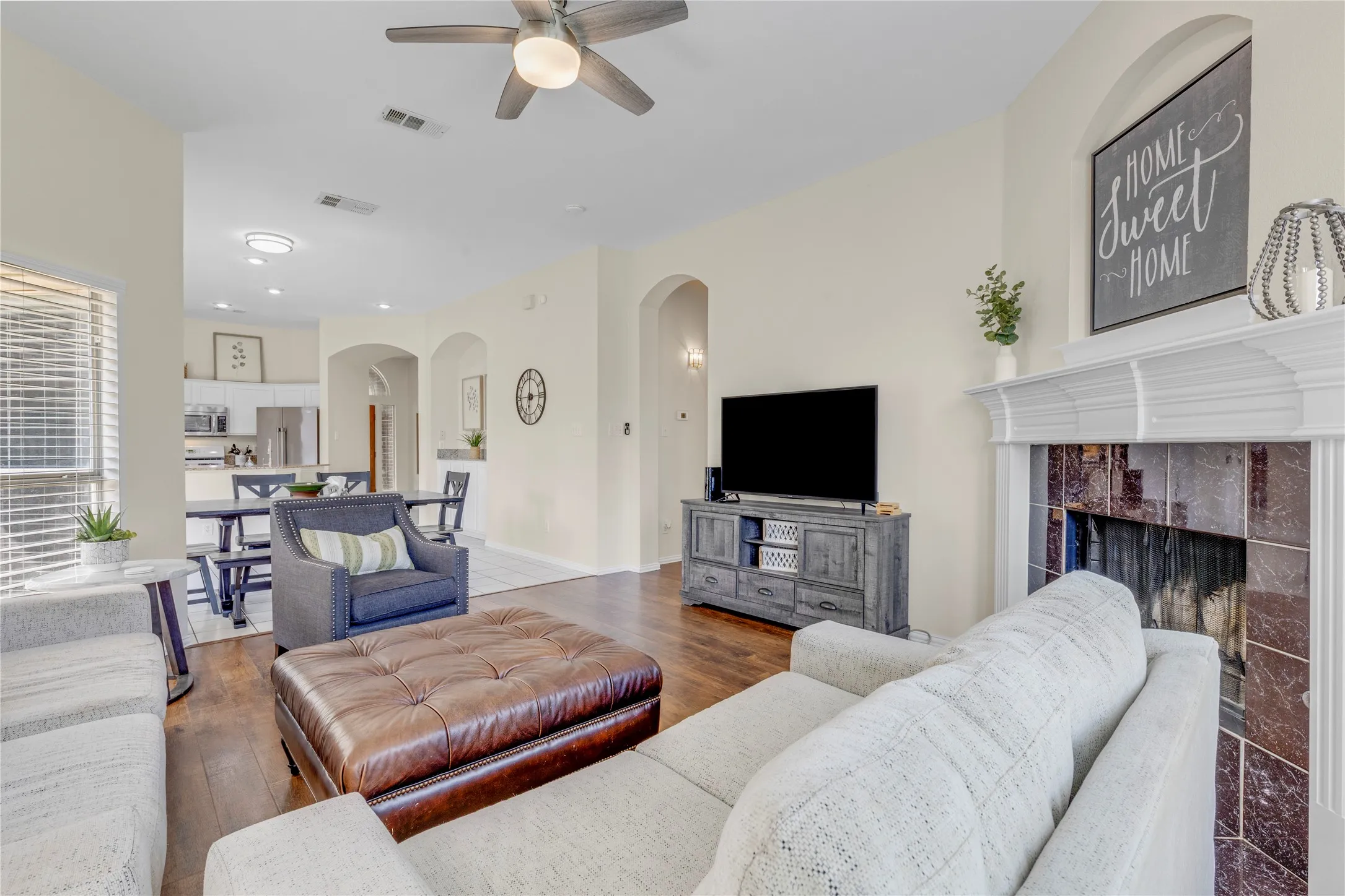 Living area with wood-finish flooring, a fireplace featuring a decorative mantel and tile surround, and an overhead ceiling fan