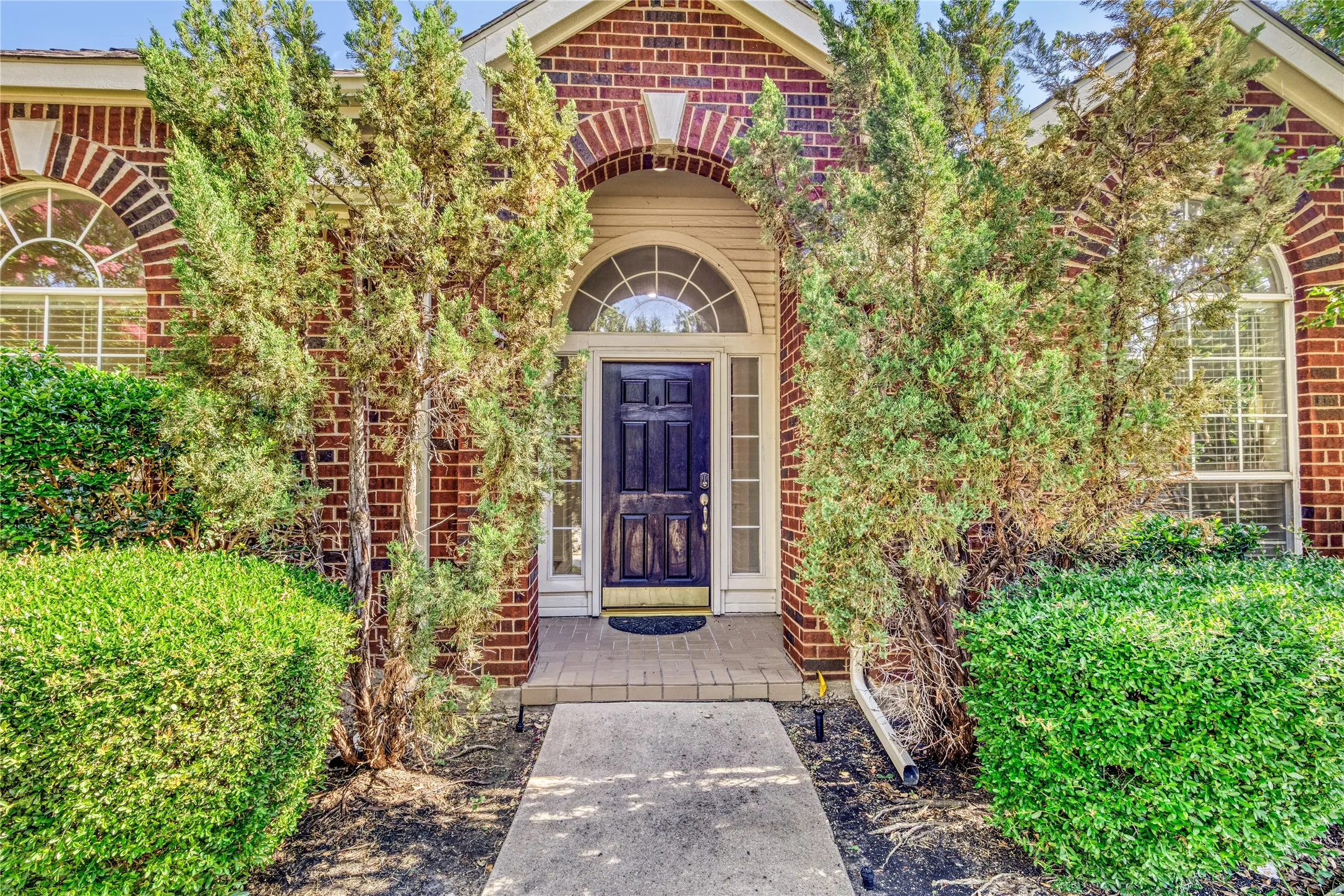 Brick exterior with arched window details, formal entry door with sidelights, and mature front landscaping