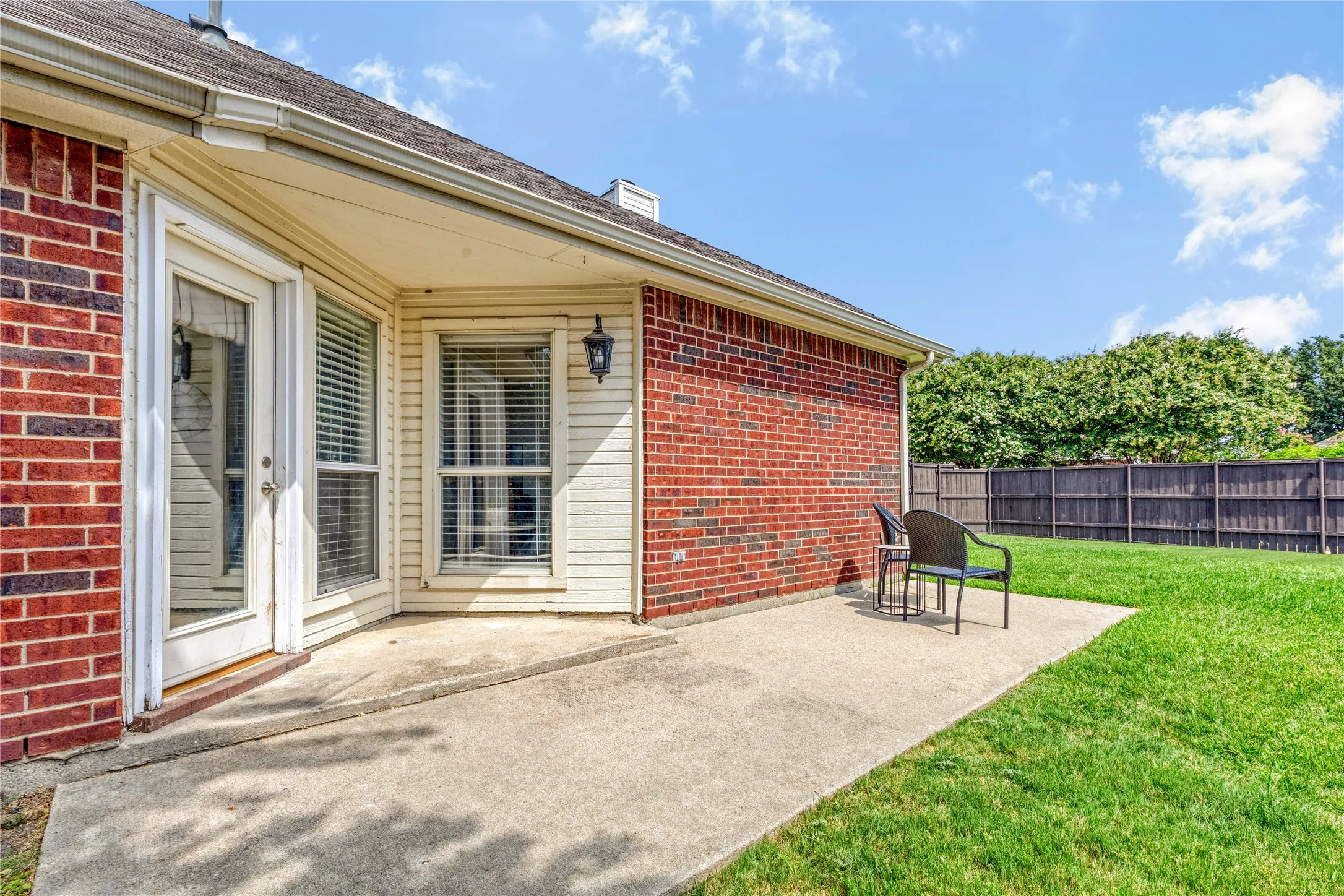 Brick exterior with light-colored siding, concrete patio, and a grass lawn with a wood fence