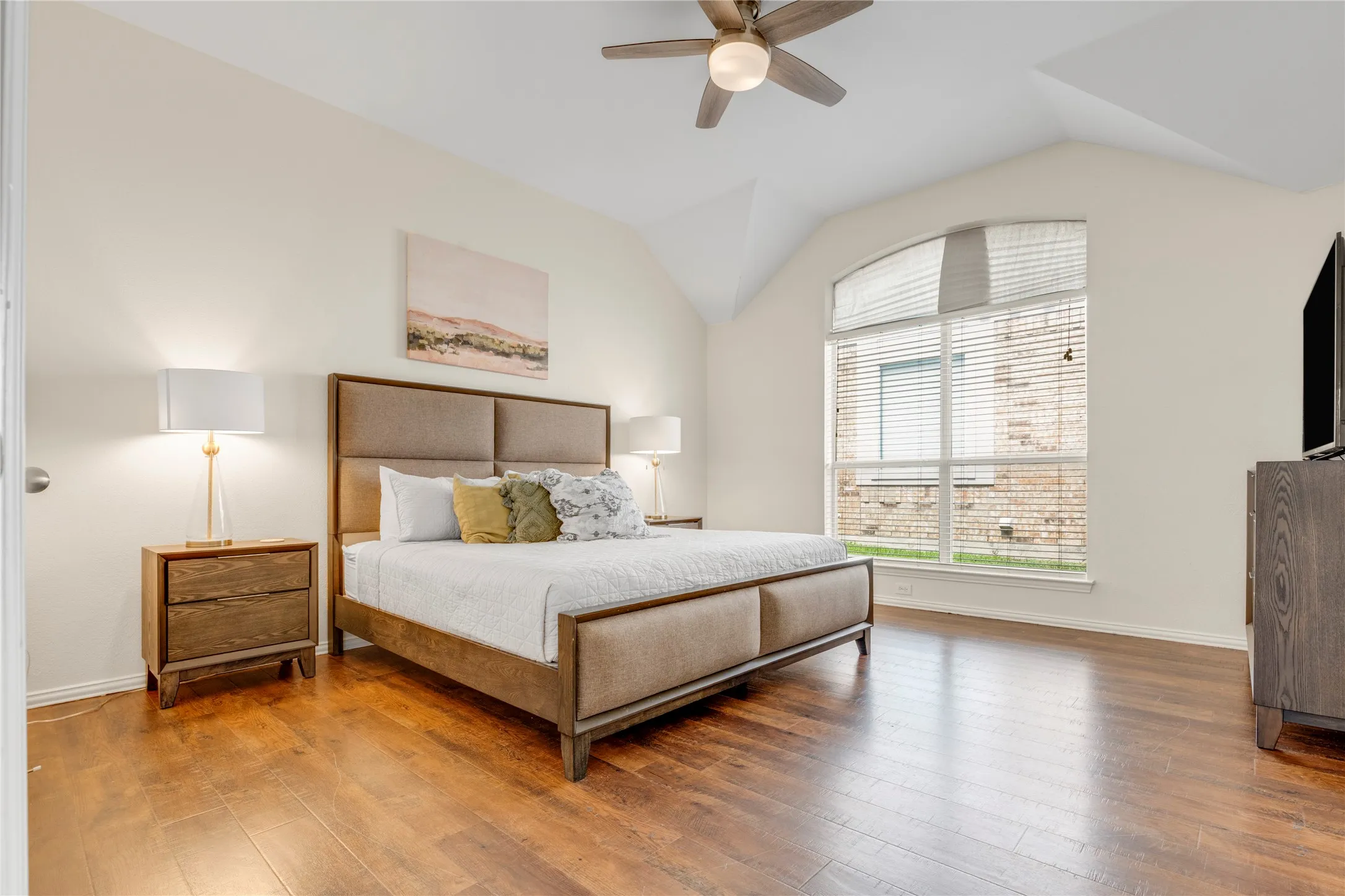 Vaulted ceiling, wood-finish flooring, arched window with blinds, and ceiling fan with integrated lighting