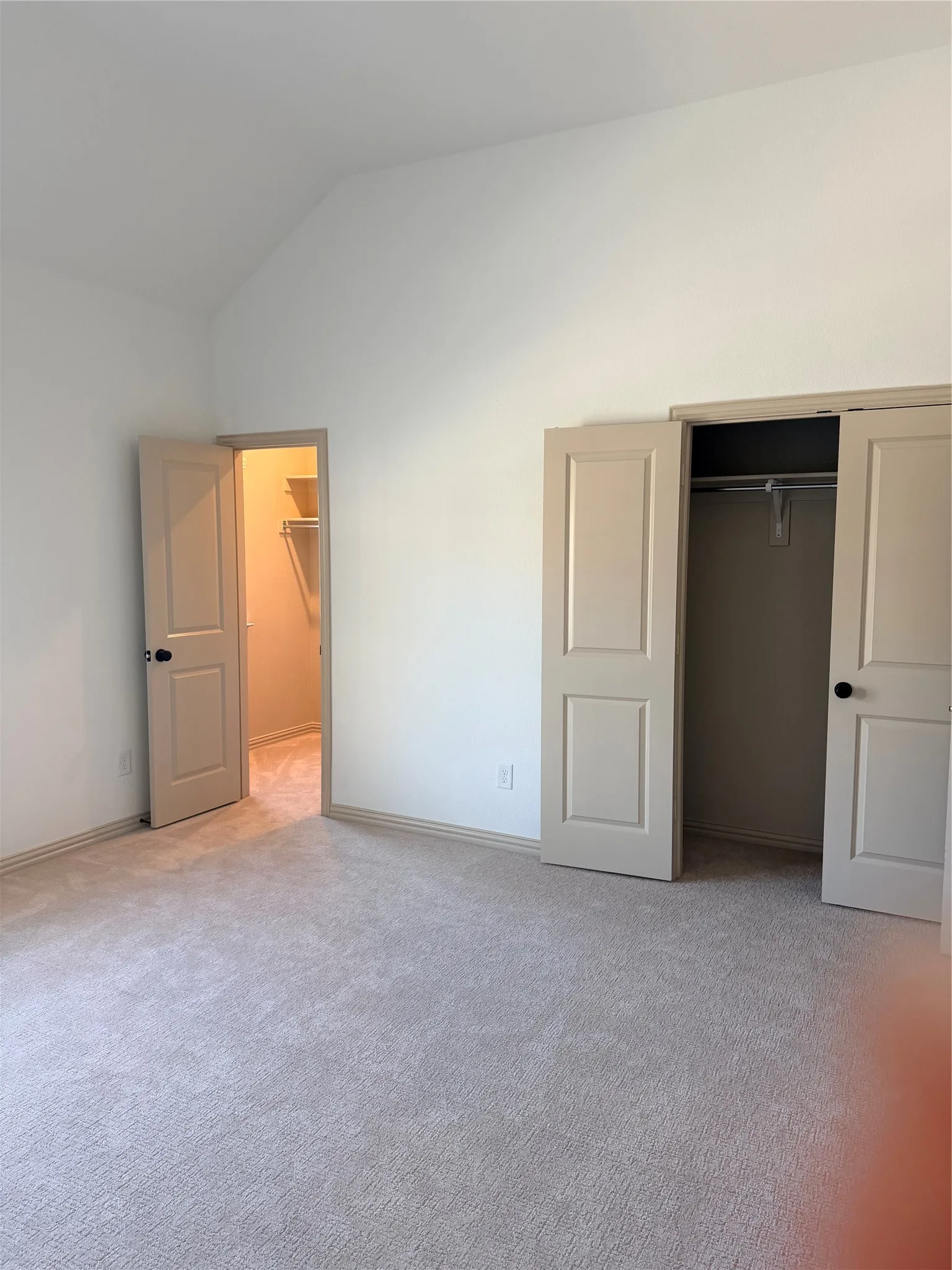 Master Bedroom wiVaulted ceiling, neutral wall paint, light-colored carpet, hinged bi-fold closet doors, and wood trim molding