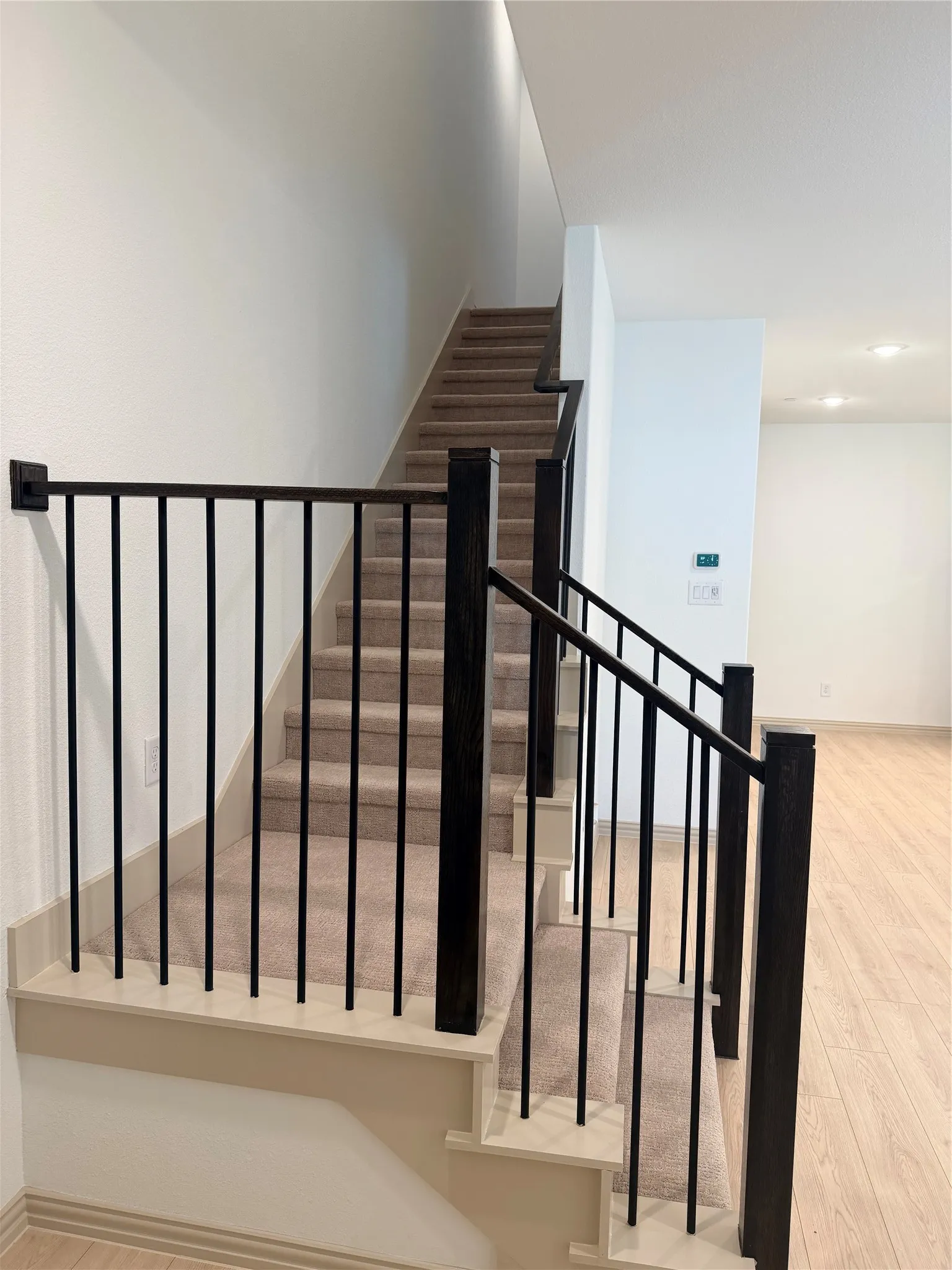 Carpeted staircase featuring black metal balusters and wood newel posts