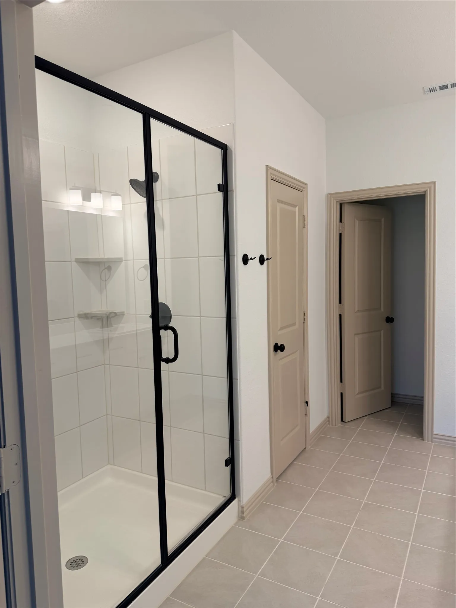 Walk-in shower with black-framed glass enclosure, white subway tile surround, and built-in shower shelf