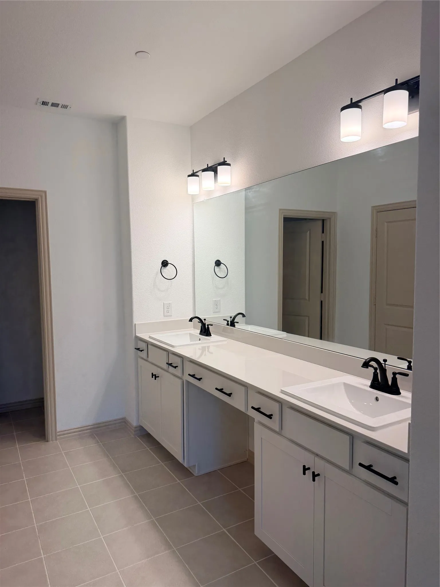 Dual vanities with white countertops, integrated sinks, black fixtures, and white cabinetry
