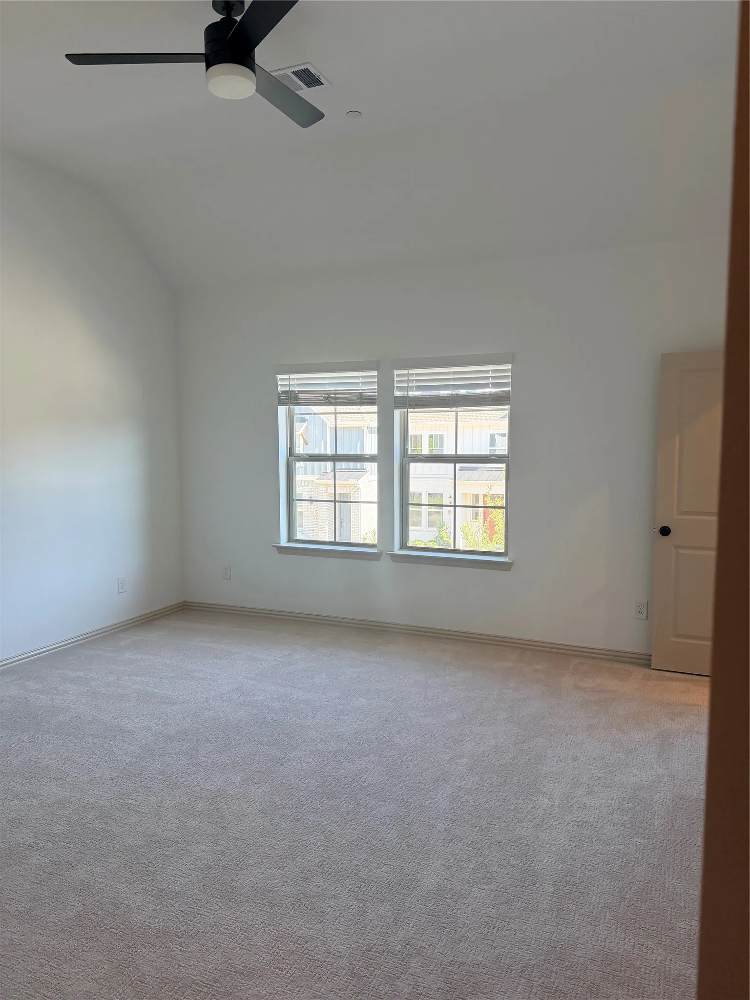 Spacious room with vaulted ceilings, neutral-toned carpet, and a modern ceiling fan