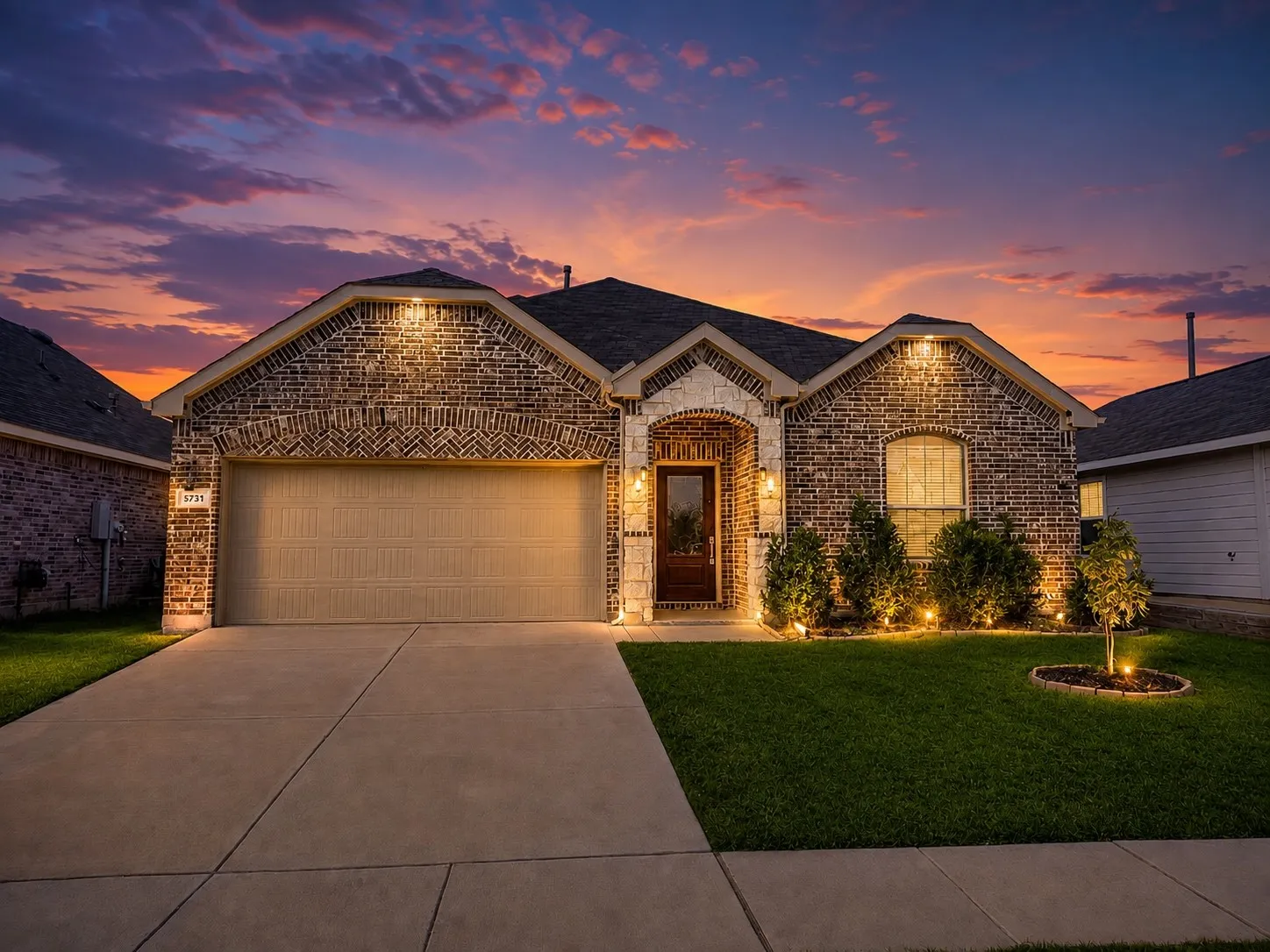 Brick and stone facade, arched entry, integrated garage, mature landscaping, and exterior architectural lighting