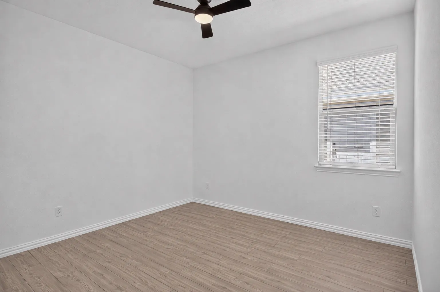 Wood-finish flooring, white painted walls, window with blinds, and a ceiling fan with integrated lighting