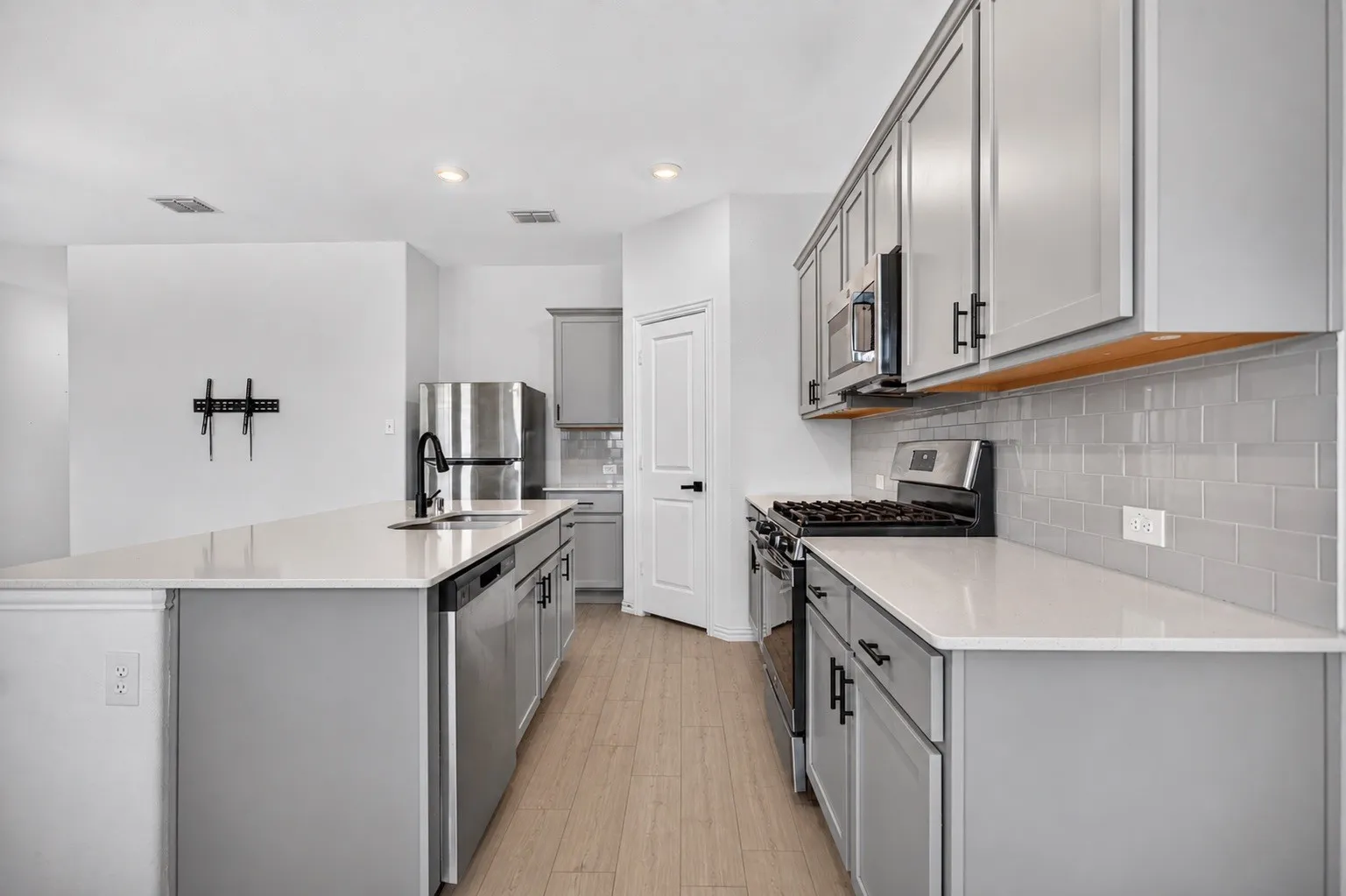 Contemporary kitchen featuring light wood-finish flooring, light gray cabinetry, stainless steel appliances, white countertops, and a gray subway tile backsplash