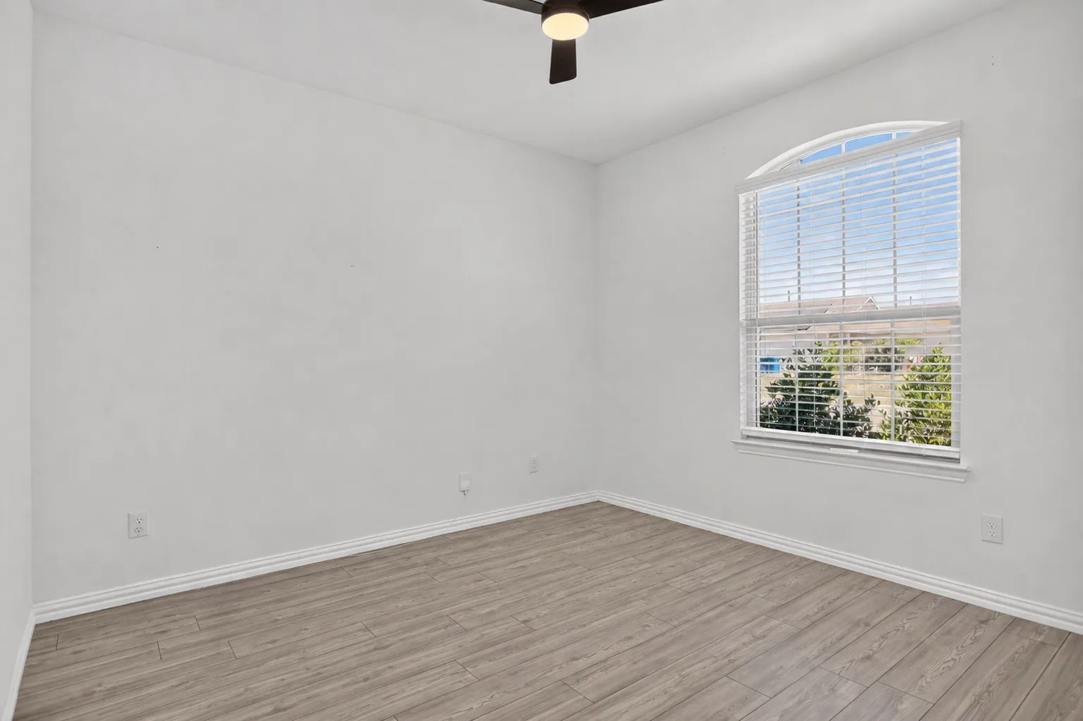Arched window with blinds, wood-finish flooring, and a ceiling fan