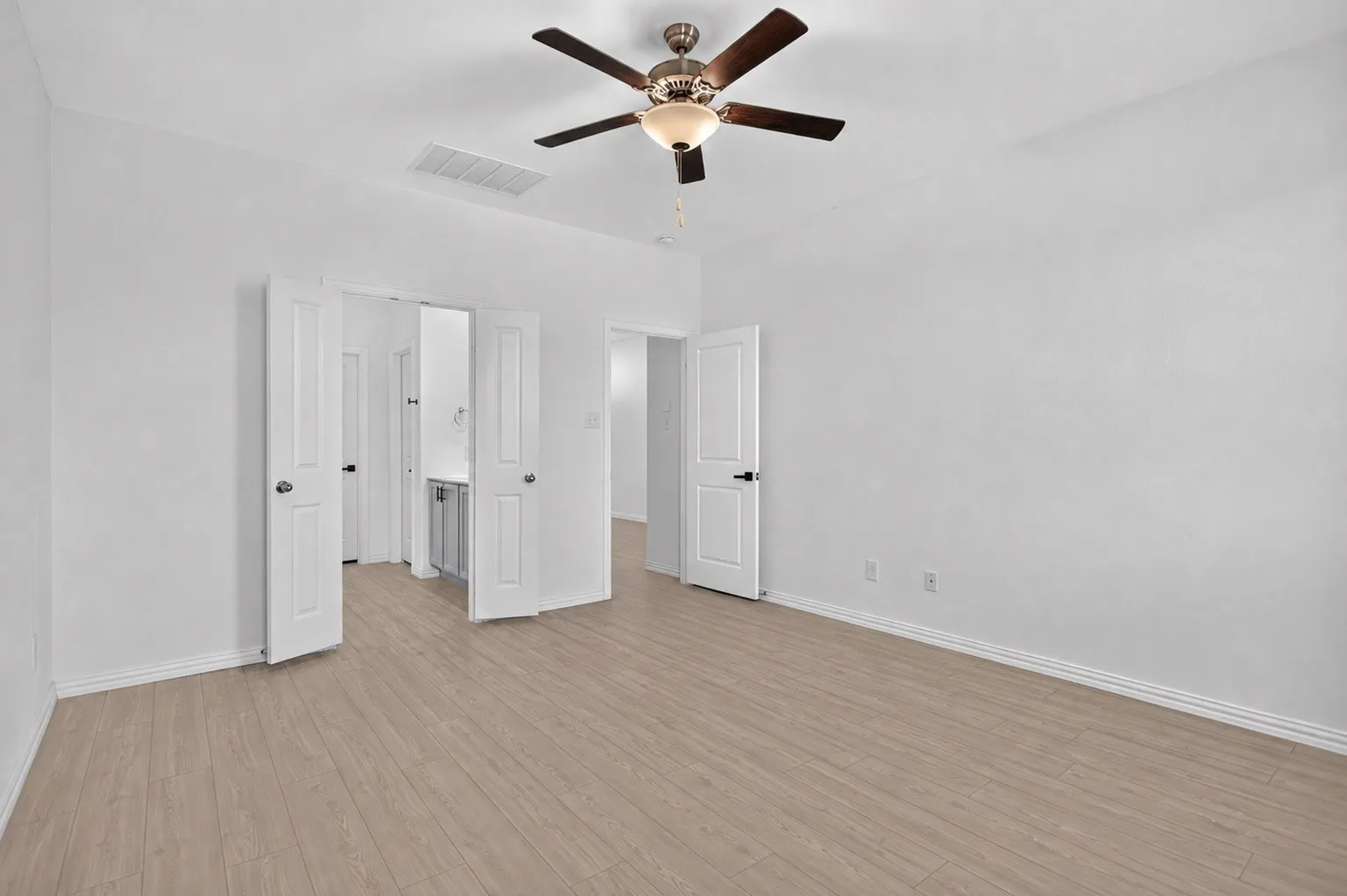 Spacious room featuring wood-finish flooring, a ceiling fan with integrated lighting, white walls, and white trim